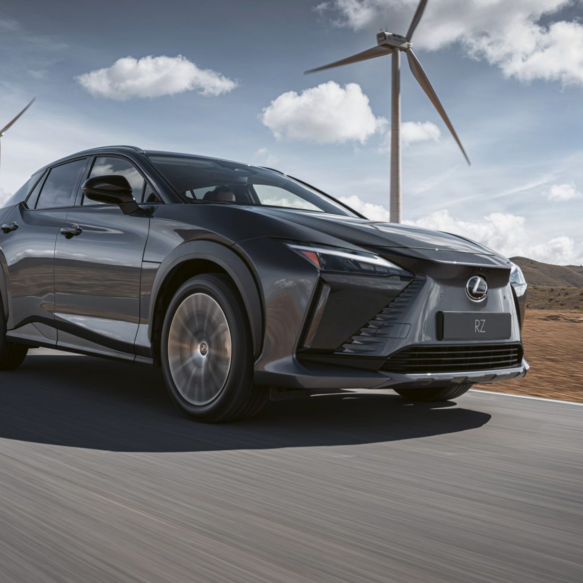 Lexus RZ 450e driving down a street with wind farms in the back