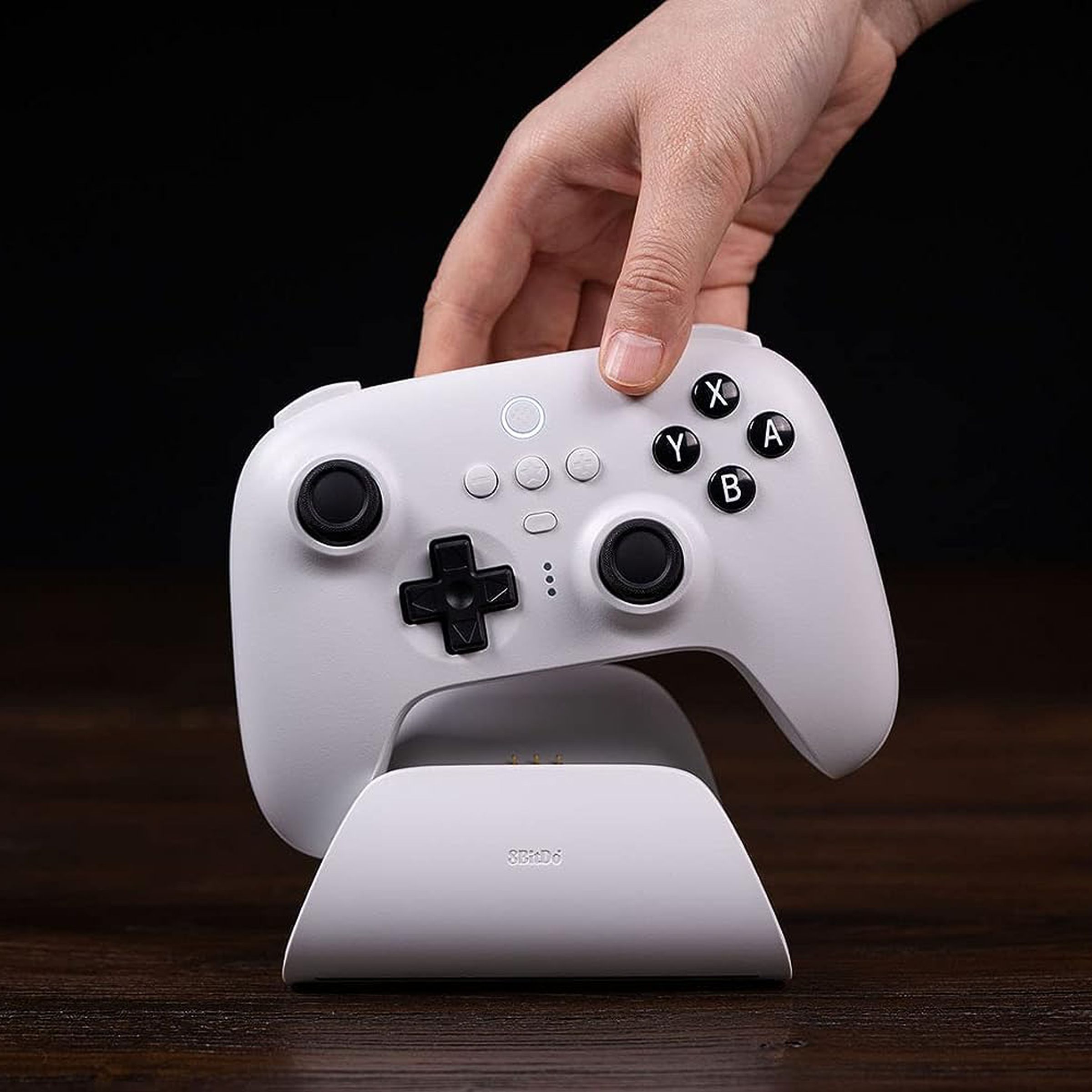 A hand picking up the white 8BitDo Ultimate Bluetooth Controller from its charging cradle.