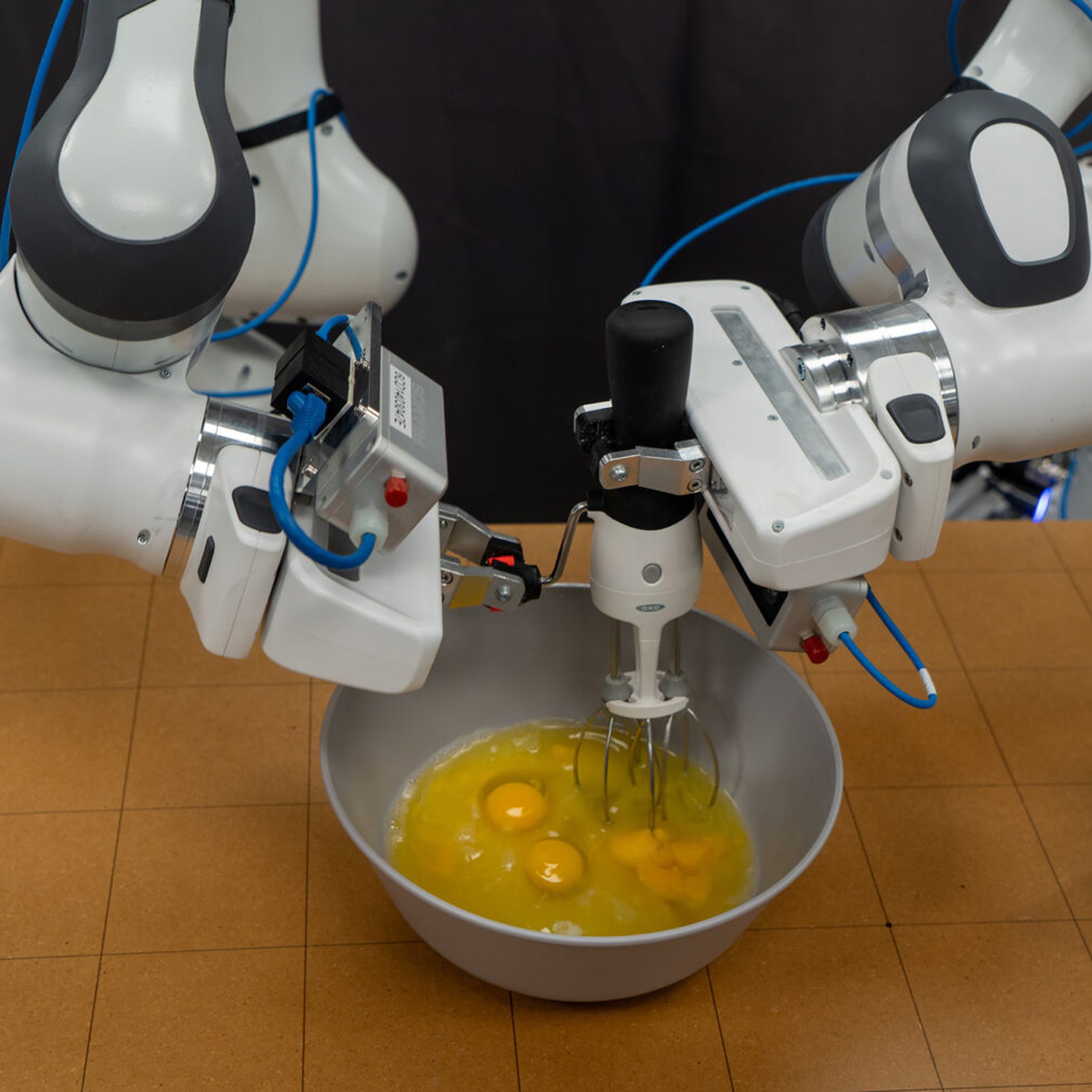 A picture of robotic arms whisking eggs in a metal bowl.