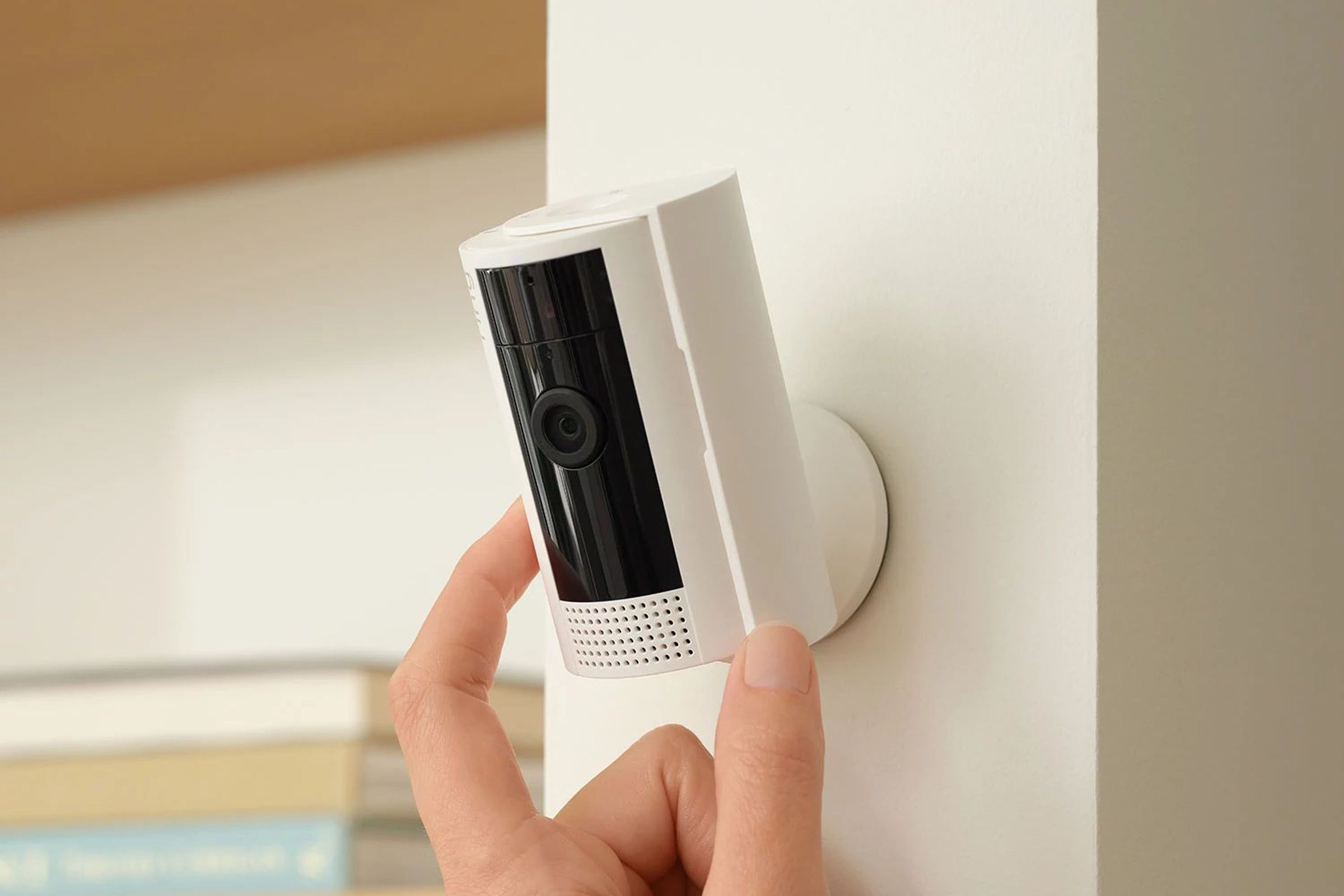 A white Ring security camera mounted on a wall with a hand adjusting it.