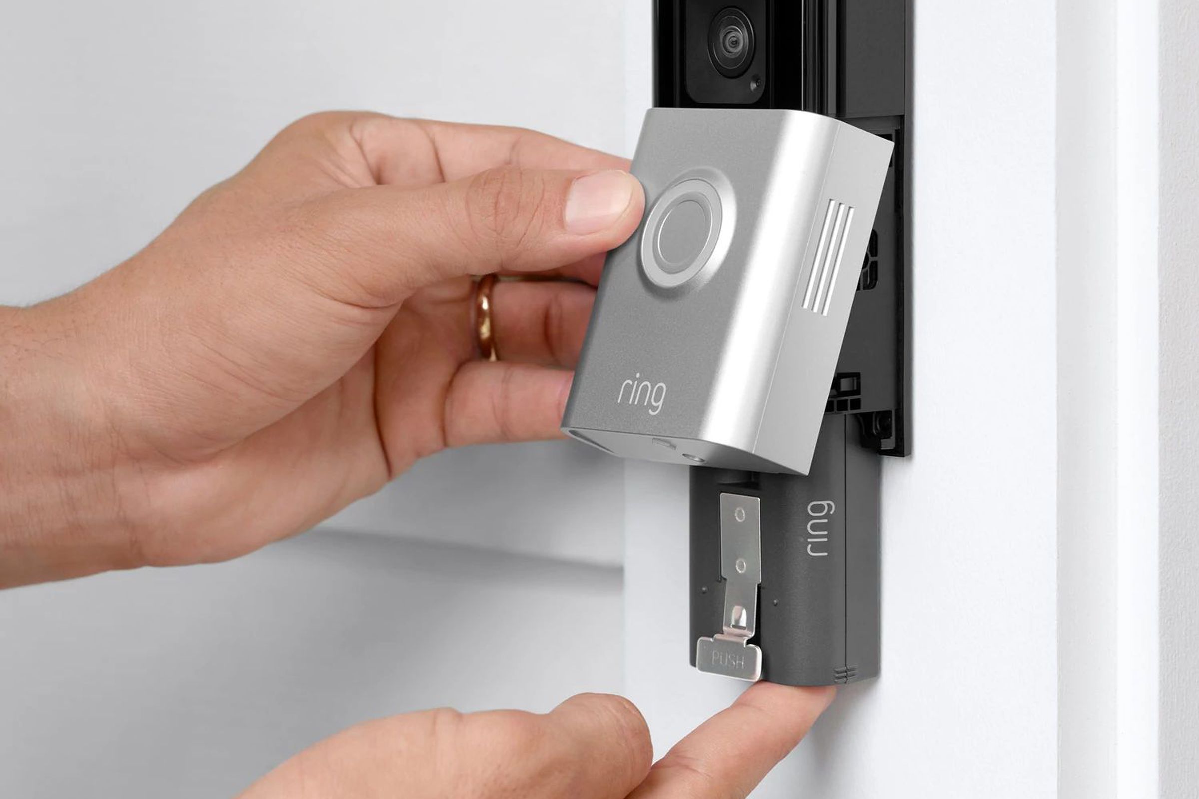A person installing a removable battery from a Ring Video Doorbell installed on a door frame.