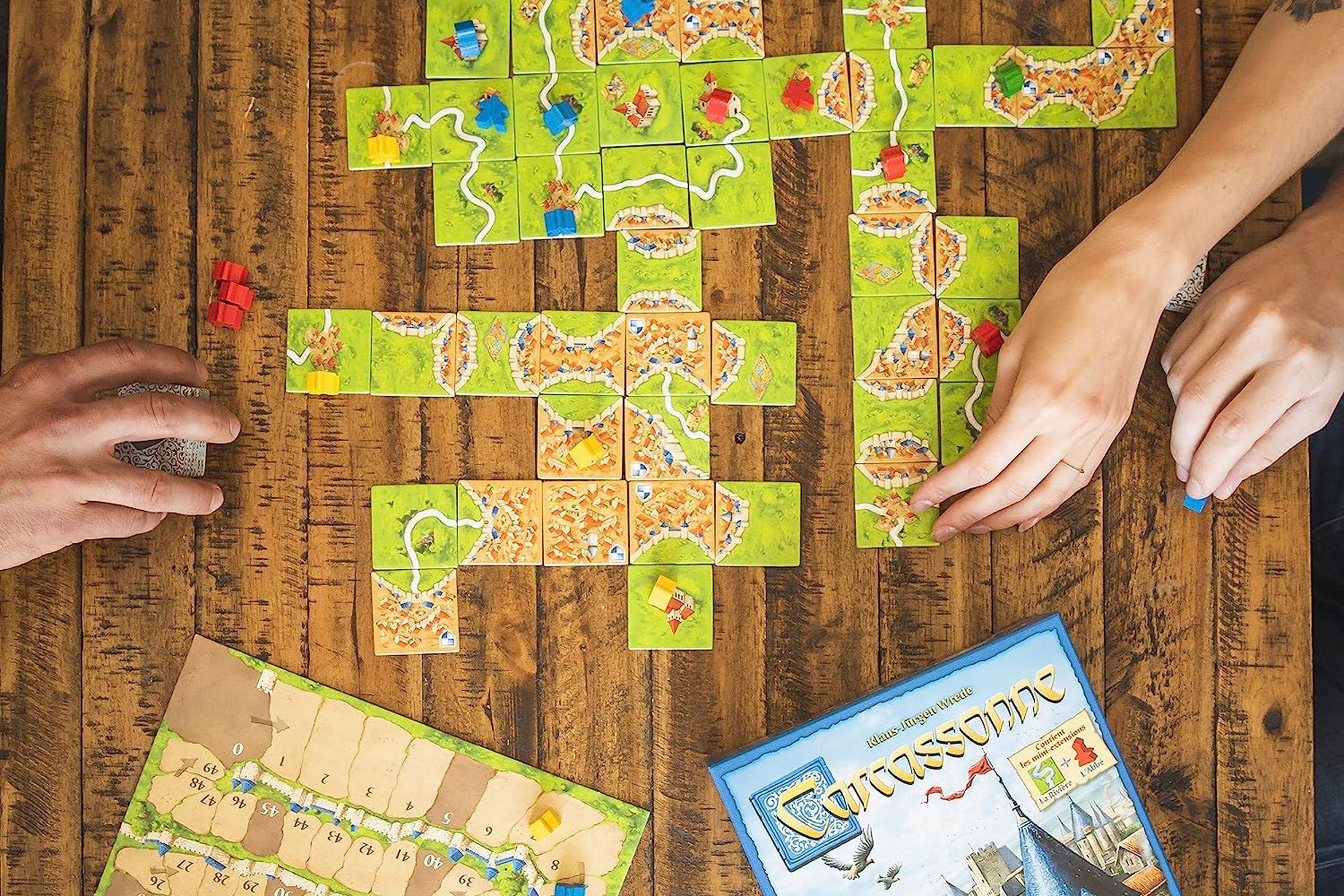 top down view of Carcassone board game with two hands laying out tiles.
