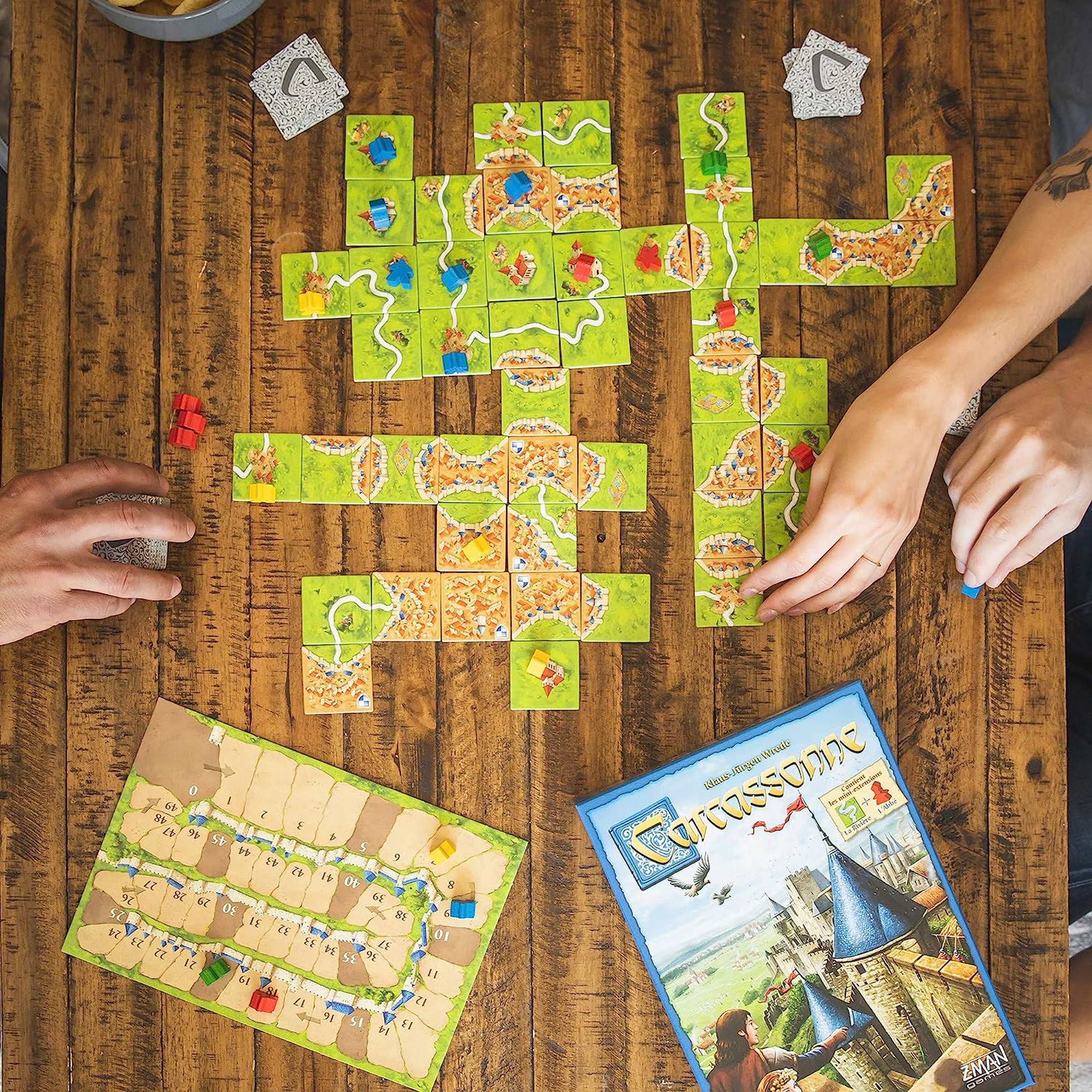 top down view of Carcassone board game with two hands laying out tiles.