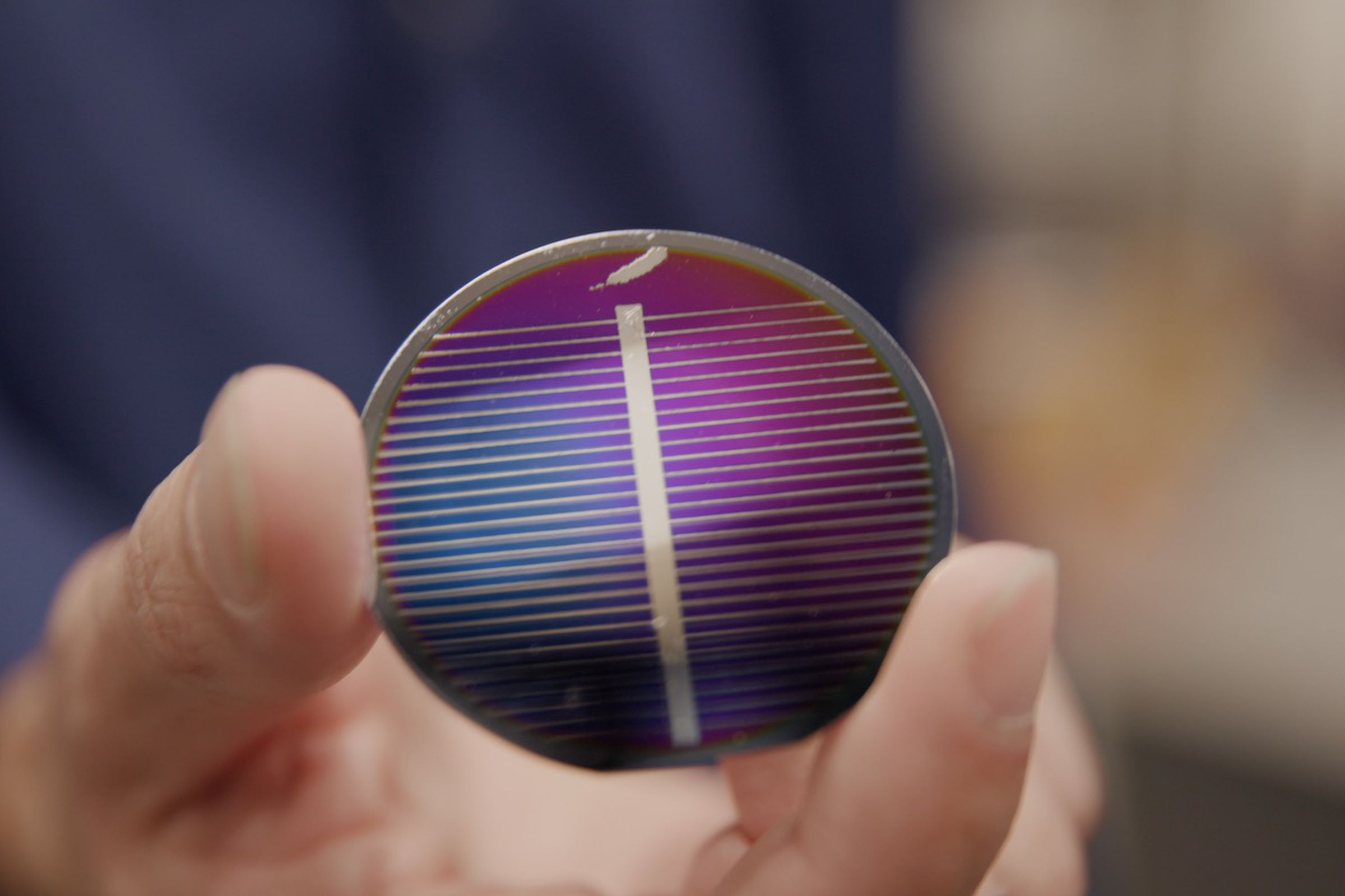 A close-up of a person’s hand holding a round solar cell.