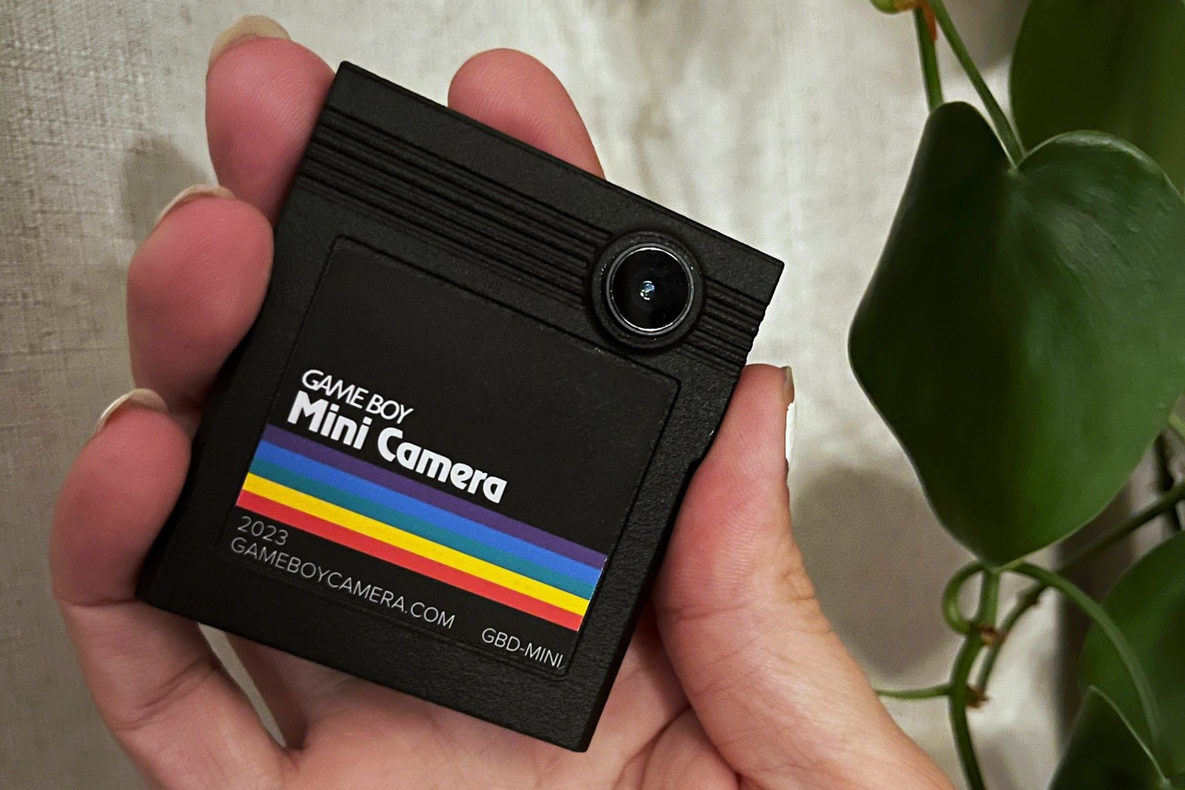 A black game boy cartridge with a rainbow stripe and an iphone lens sticking out.