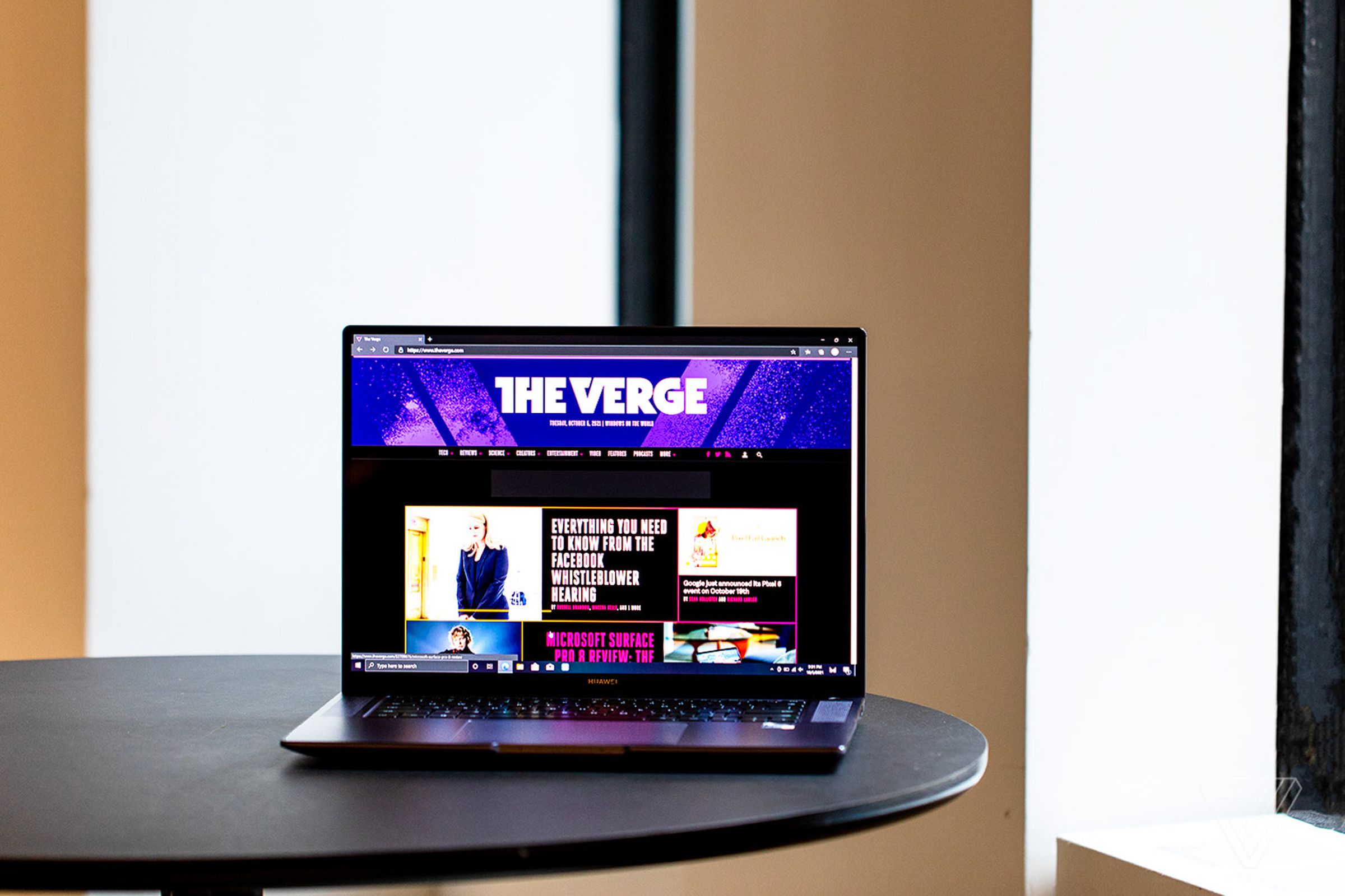 The Huawei MateBook 16 on a black table facing forward, open. The screen displays The Verge homepage.