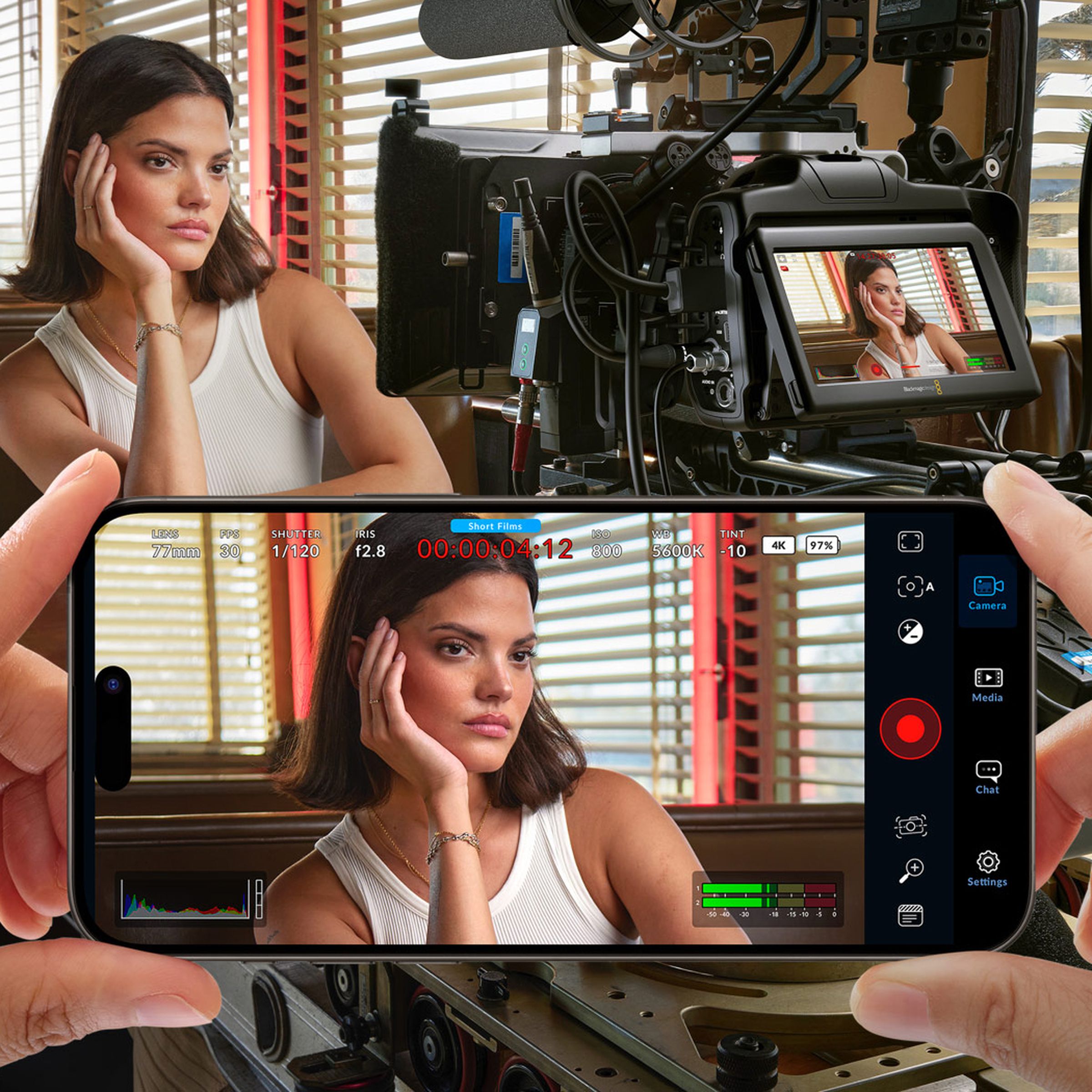 An actor in a diner is framed using the Blackmagic Camera app on a smartphone, behind a larger professional-grade camera.