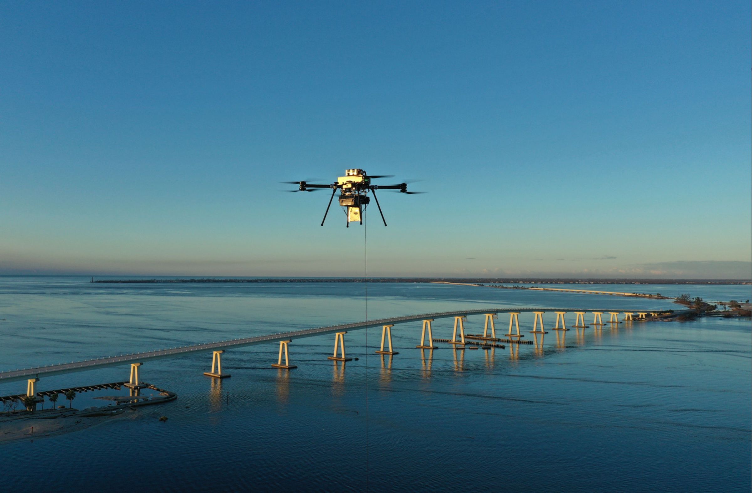 Image of a drone flying above a bridge over the ocean.