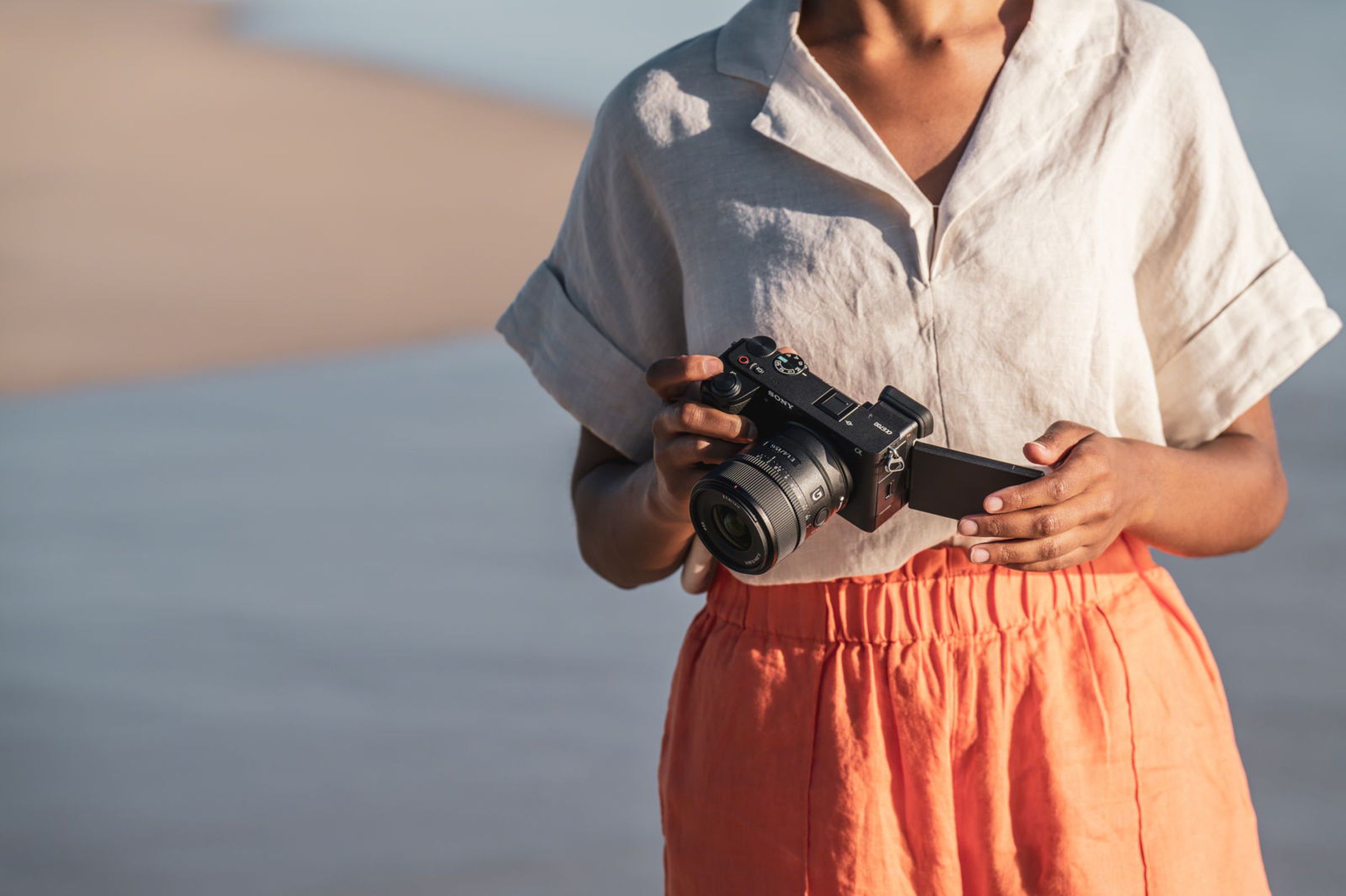 A picture of a person, standing on a beach and looking down at the camera, which has its LCD flipped out. The person’s head is not visible.