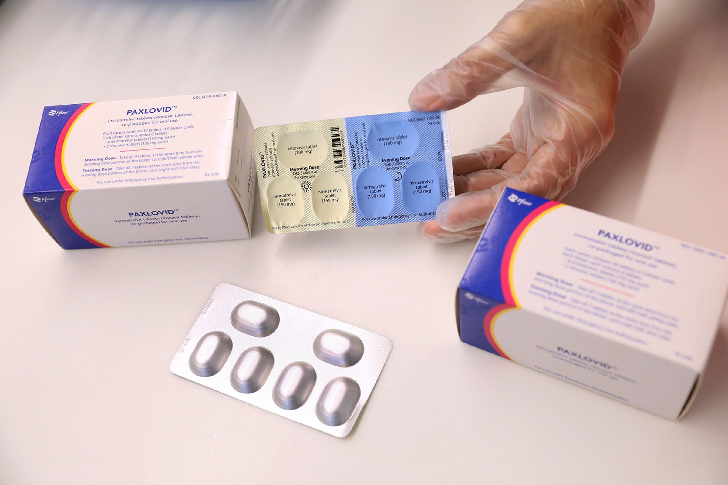 A gloved hand pulling a pill pack out of a box labeled “paxlovid”