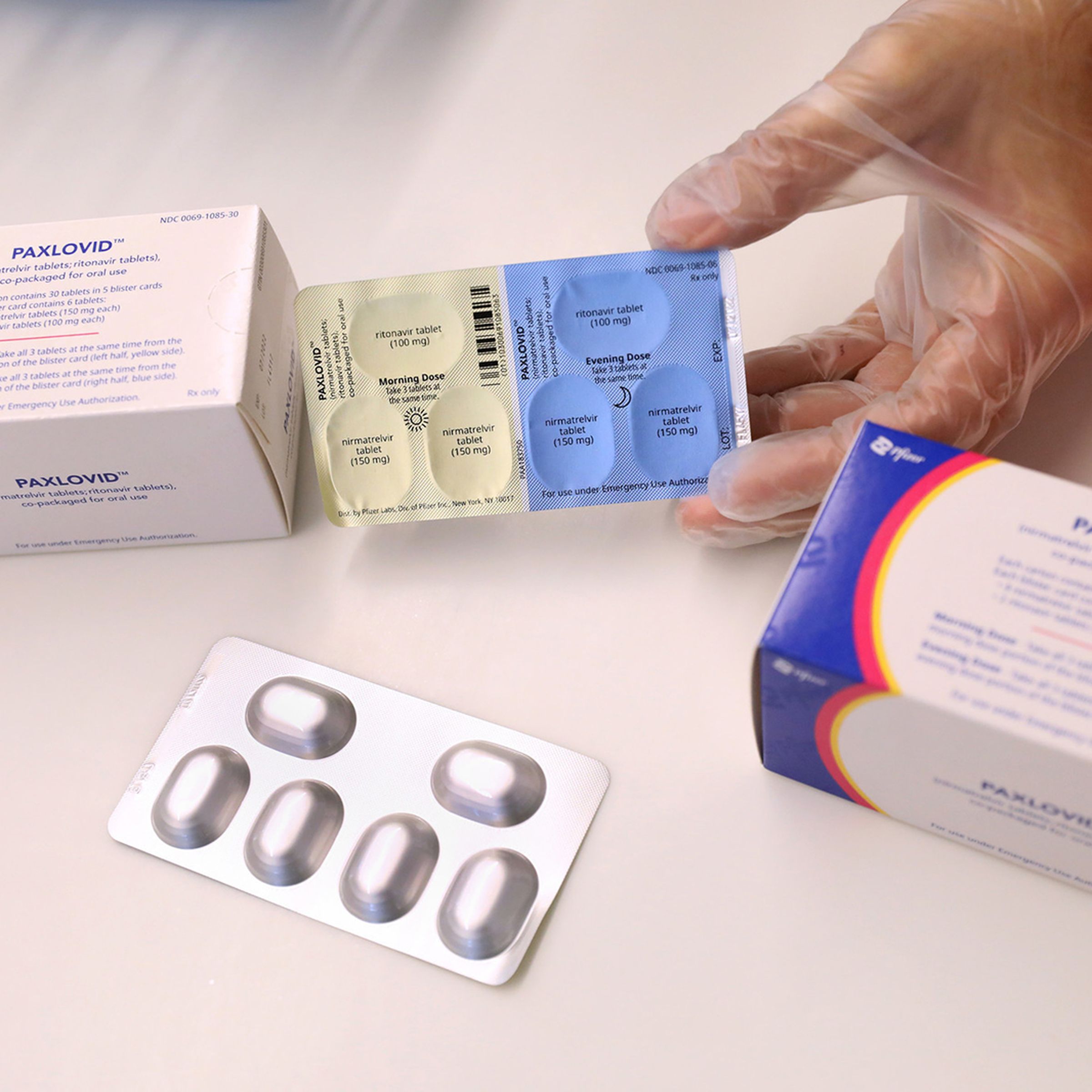 A gloved hand pulling a pill pack out of a box labeled “paxlovid”
