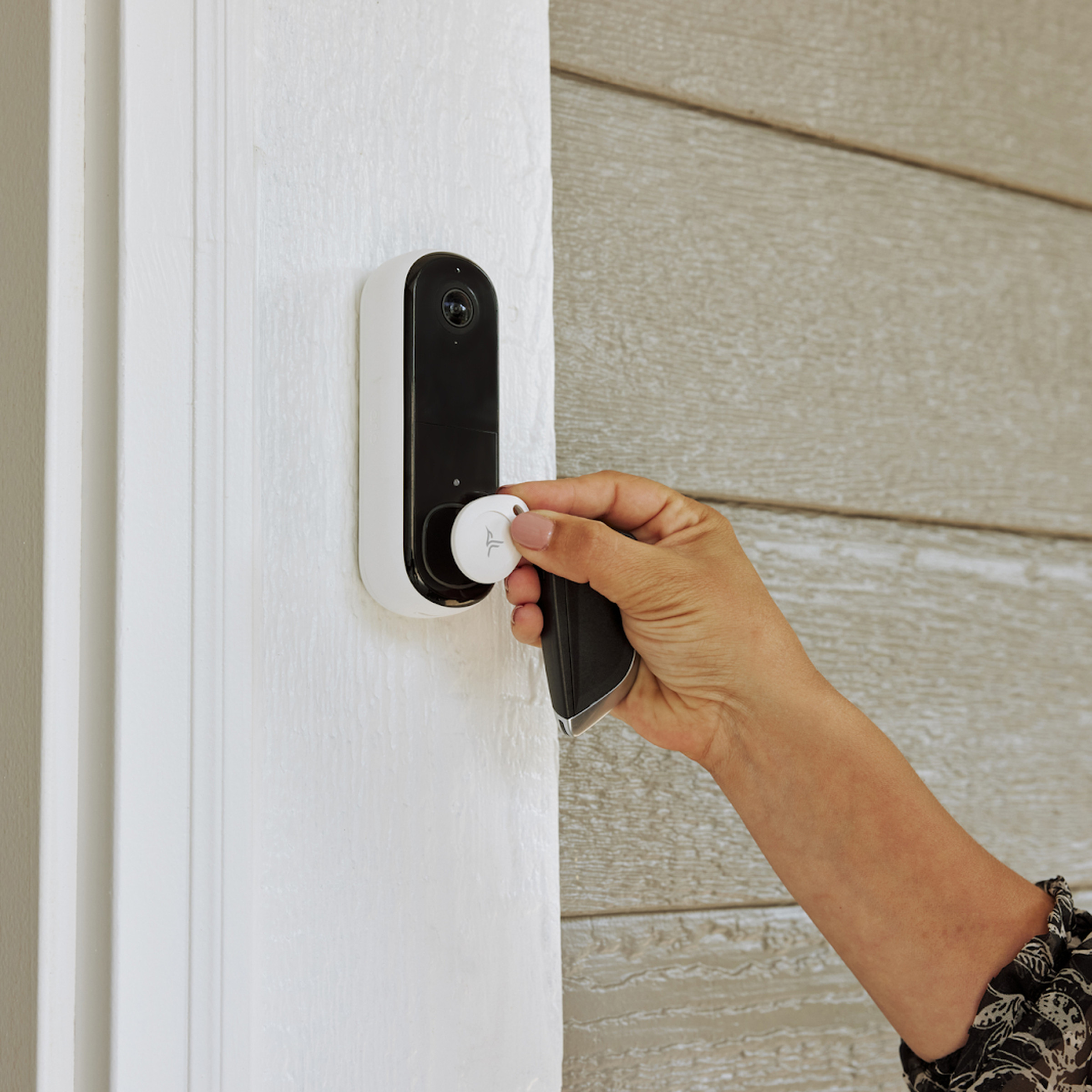 A person holding an Arlo security tag up to a doorbell.
