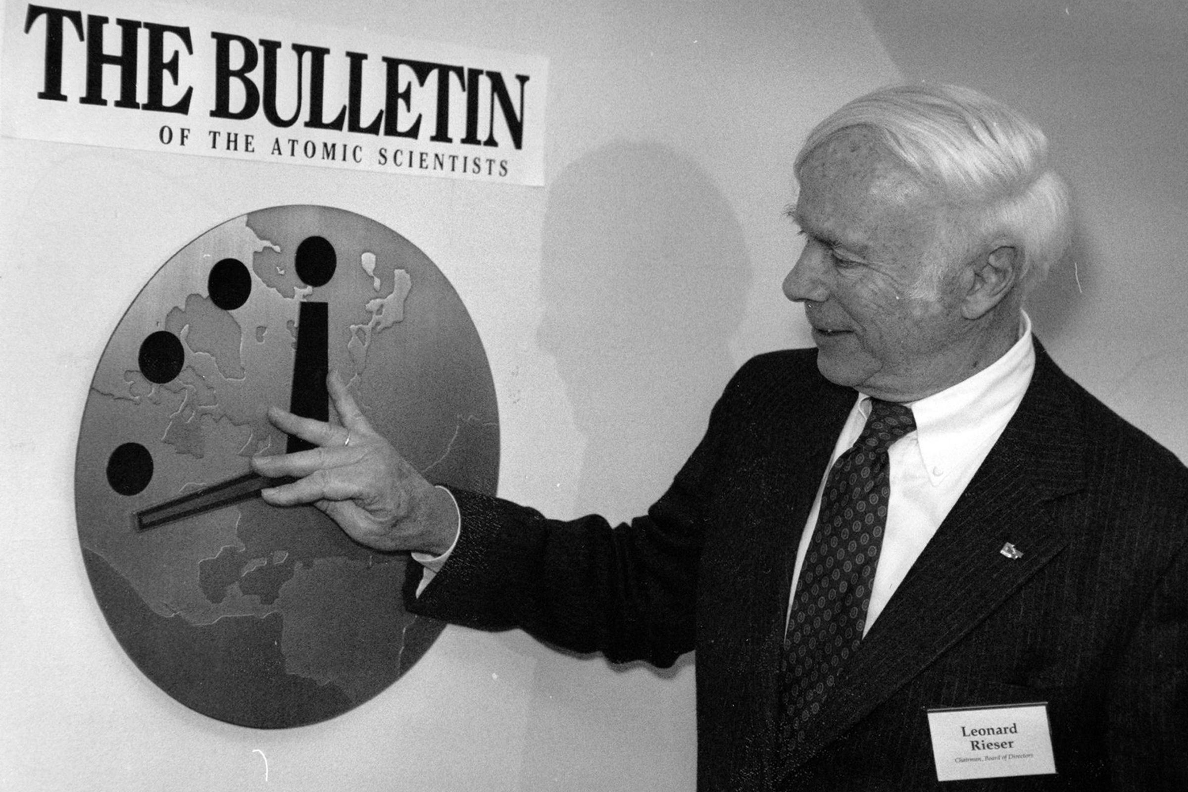 A black and white photo of a man in a suit moving the hands of the Doomsday Clock