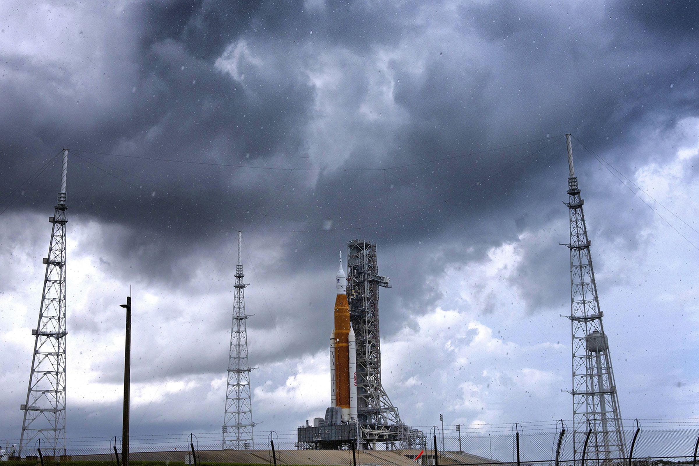 Dark clouds loom over the Artemis I rocket as it sits on a launch pad at Kennedy Space Center.