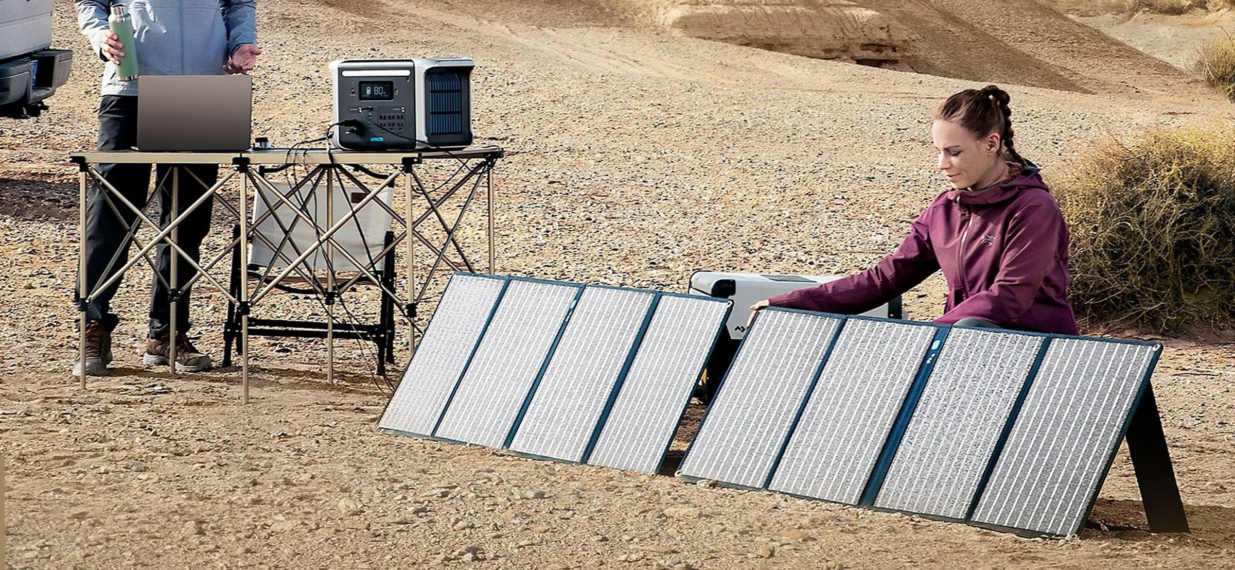 A woman kneels to set up eight solar panels in a desert