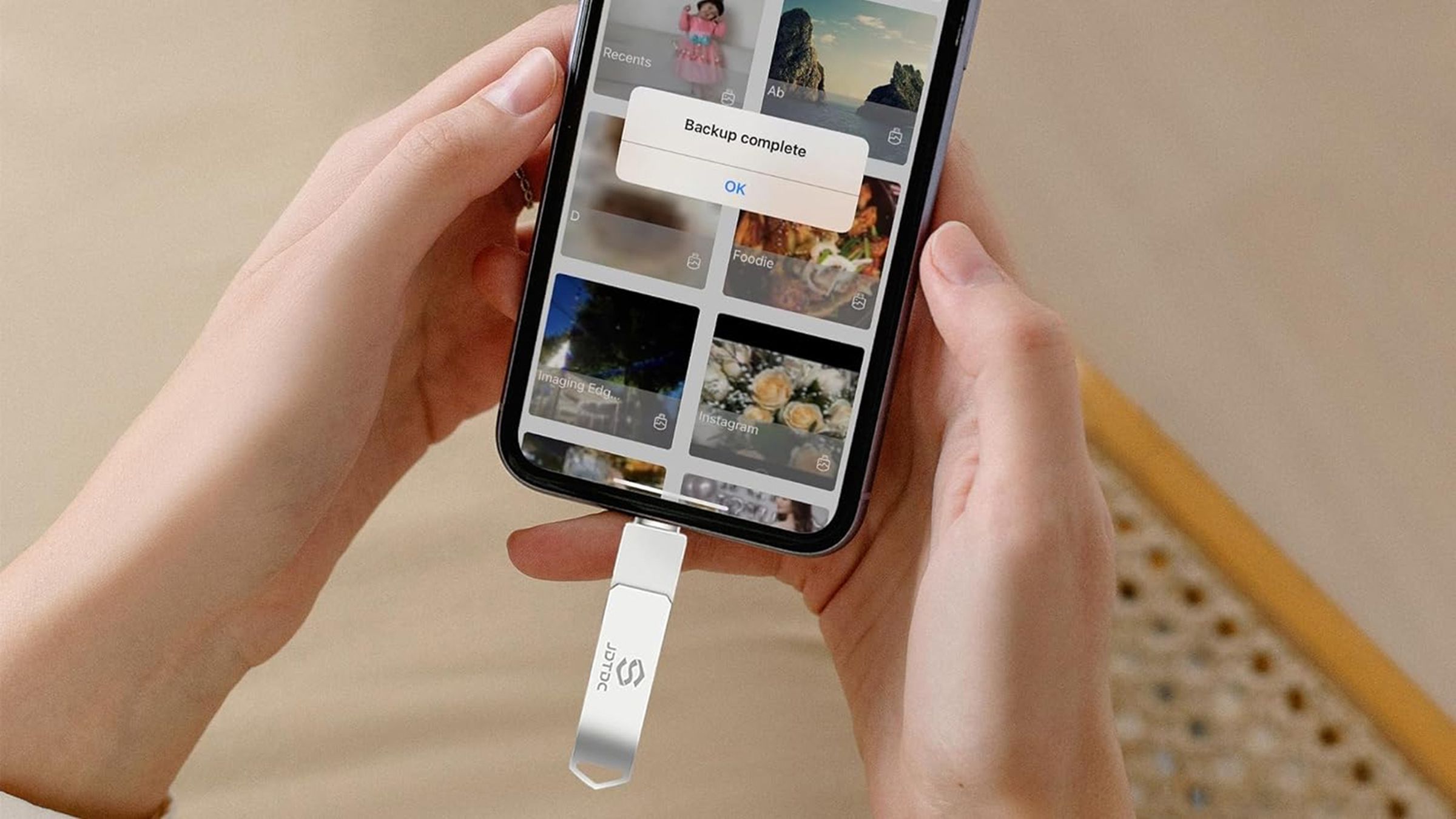 Two hands holding iPhone with thumb drive attached.