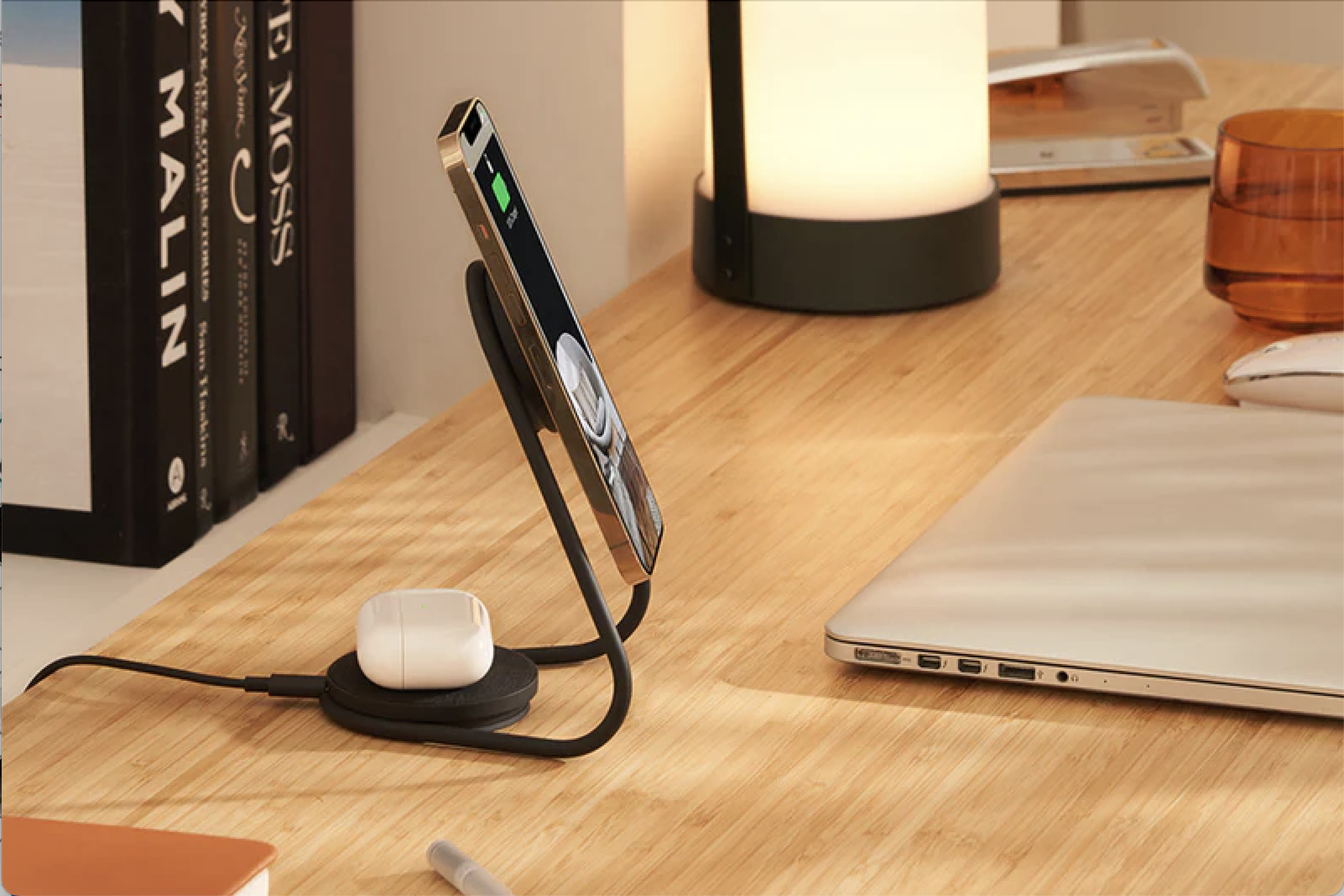 Metallic stand on a desk holding an iphone and, in back, an AirPods case.
