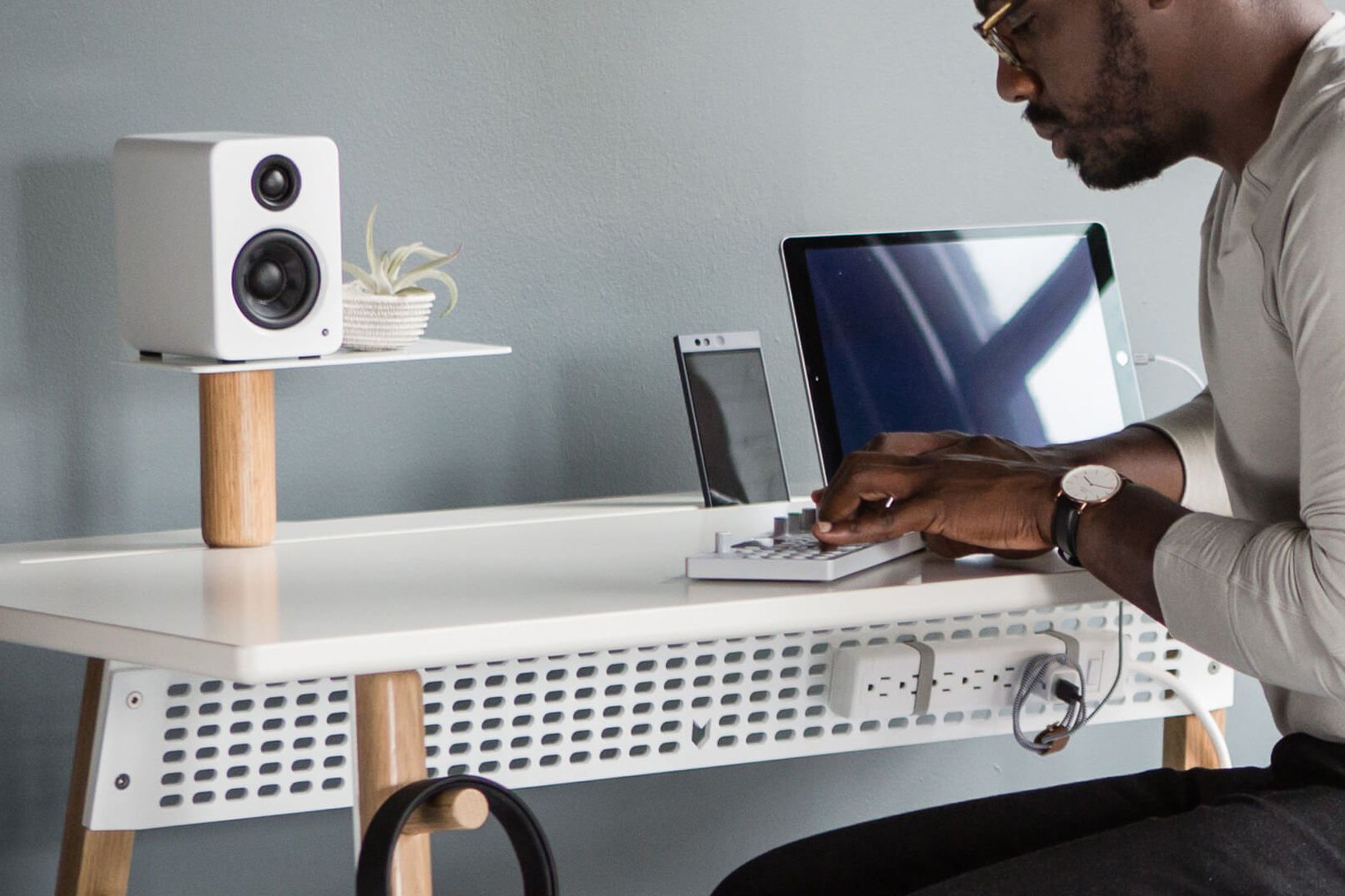The Kanto YU2 speaker sits on top of a desk while an artist composes sounds with an electronic instrument.