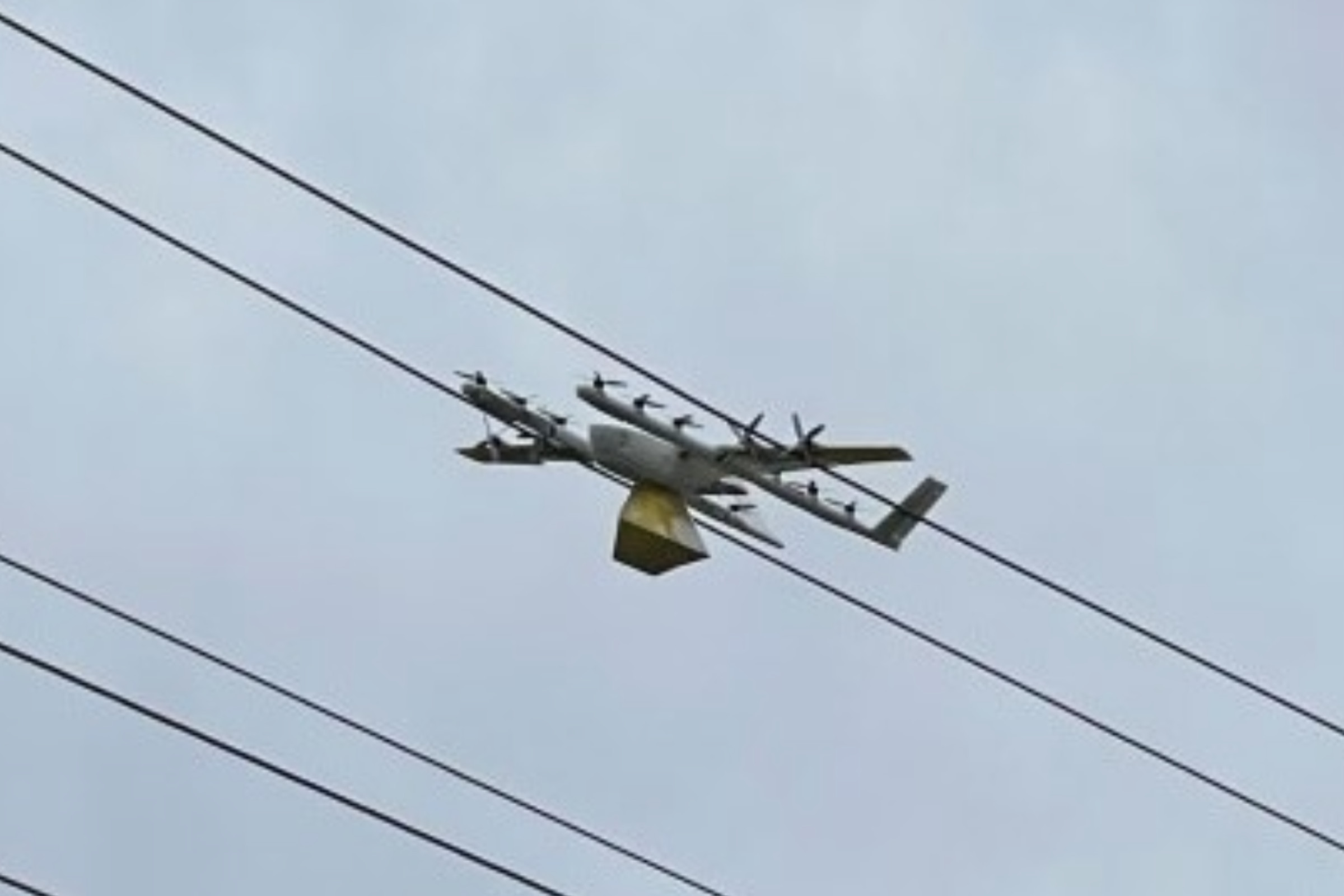 A photo showing a small drone sitting on top of overhead power lines. 