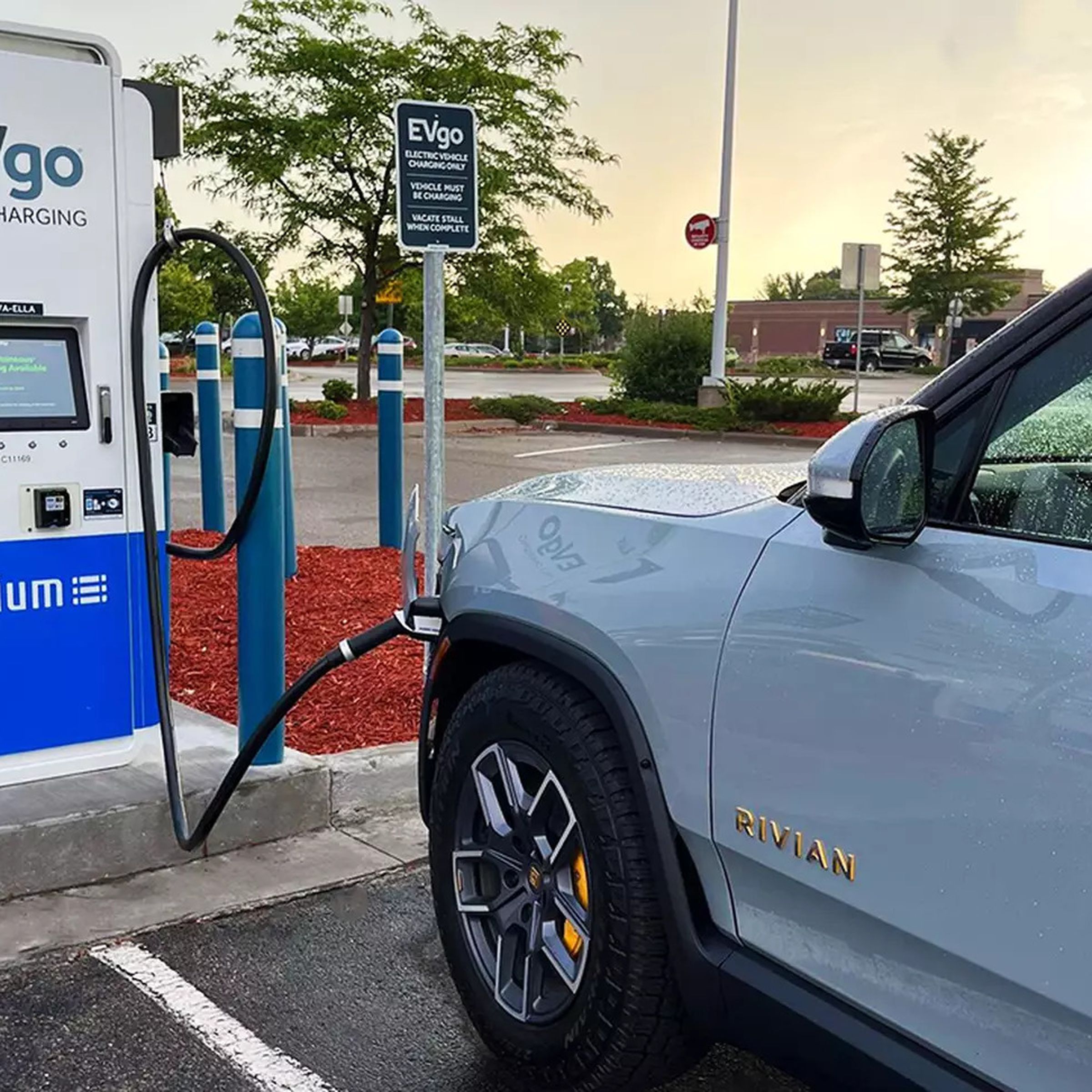 Blue Rivian truck plugged into EVgo dc fast charging station in retail parking lot