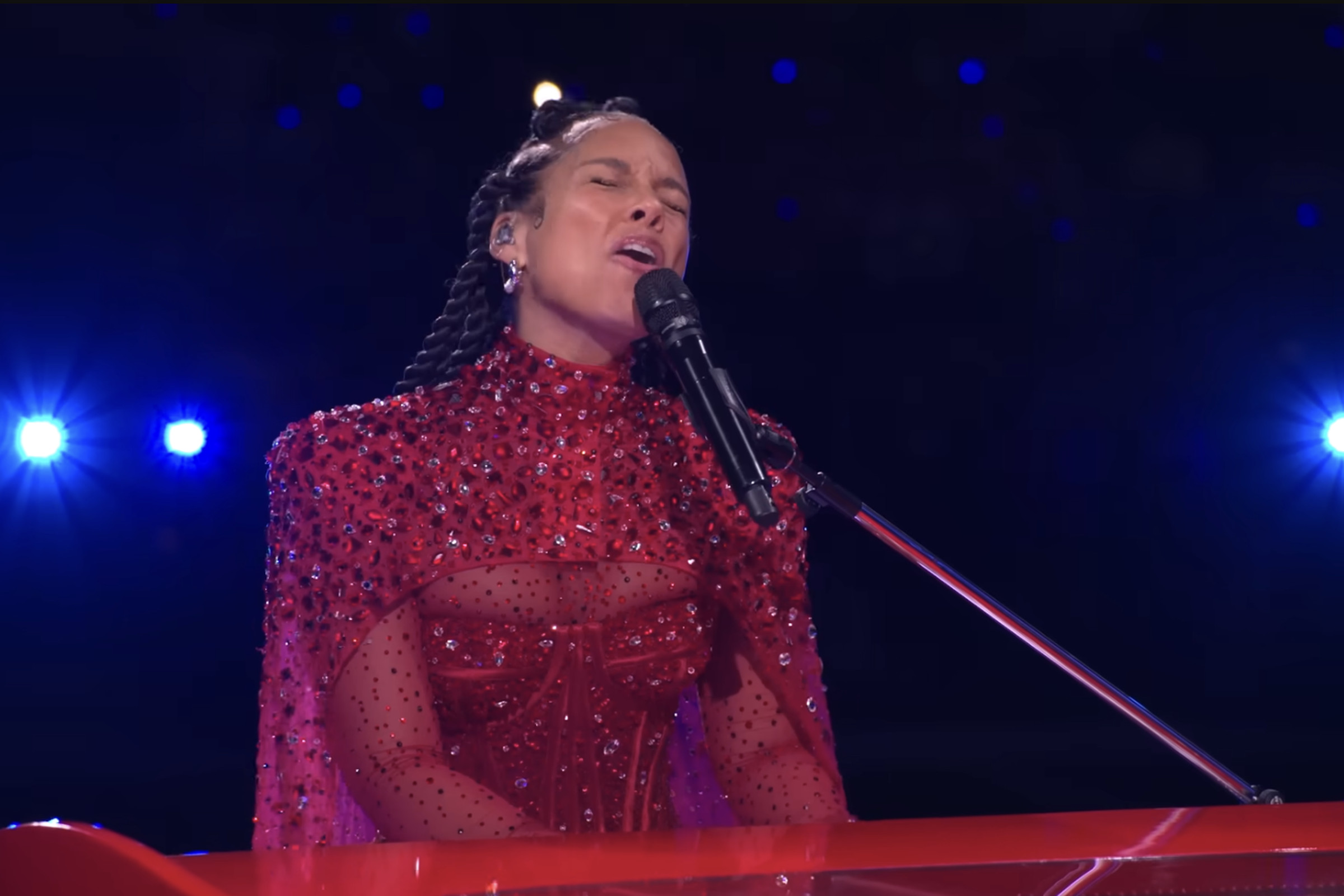 Alicia Keys at the Super Bowl 2024 Halftime show, singing into a microphone while playing piano.