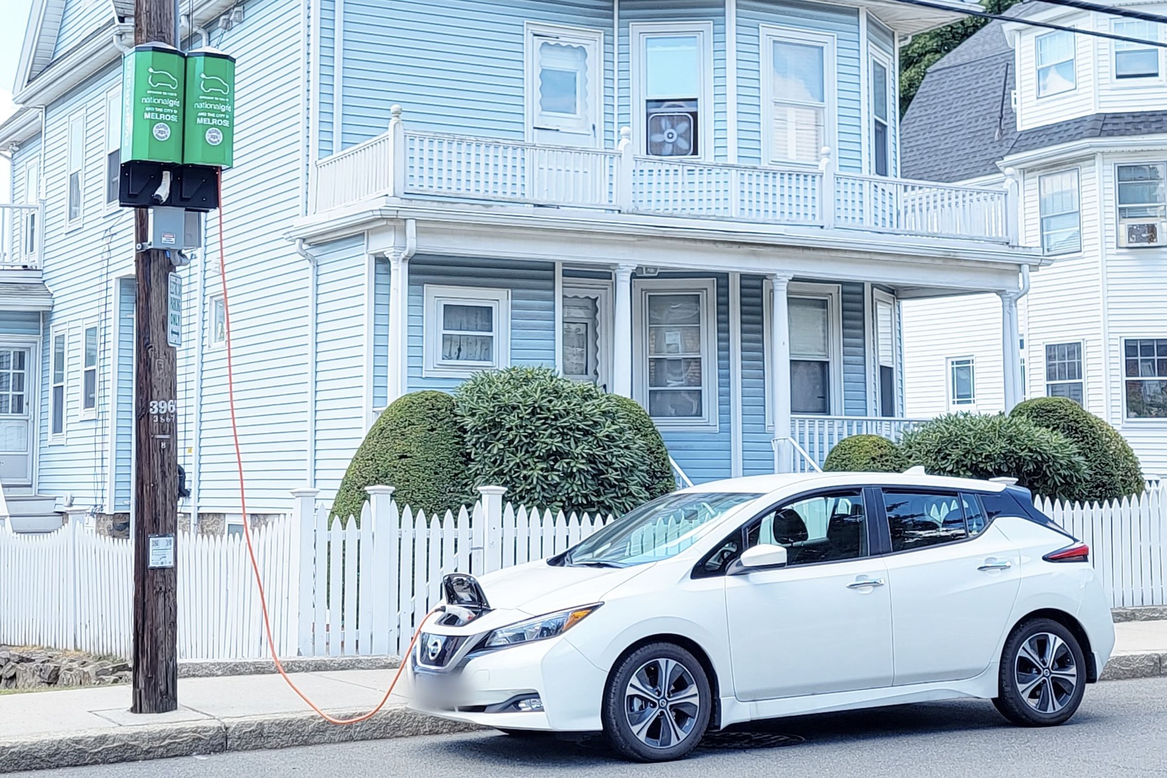 A Nissan Leaf being fed from a pole-mounted EV charger in Melrose, MA