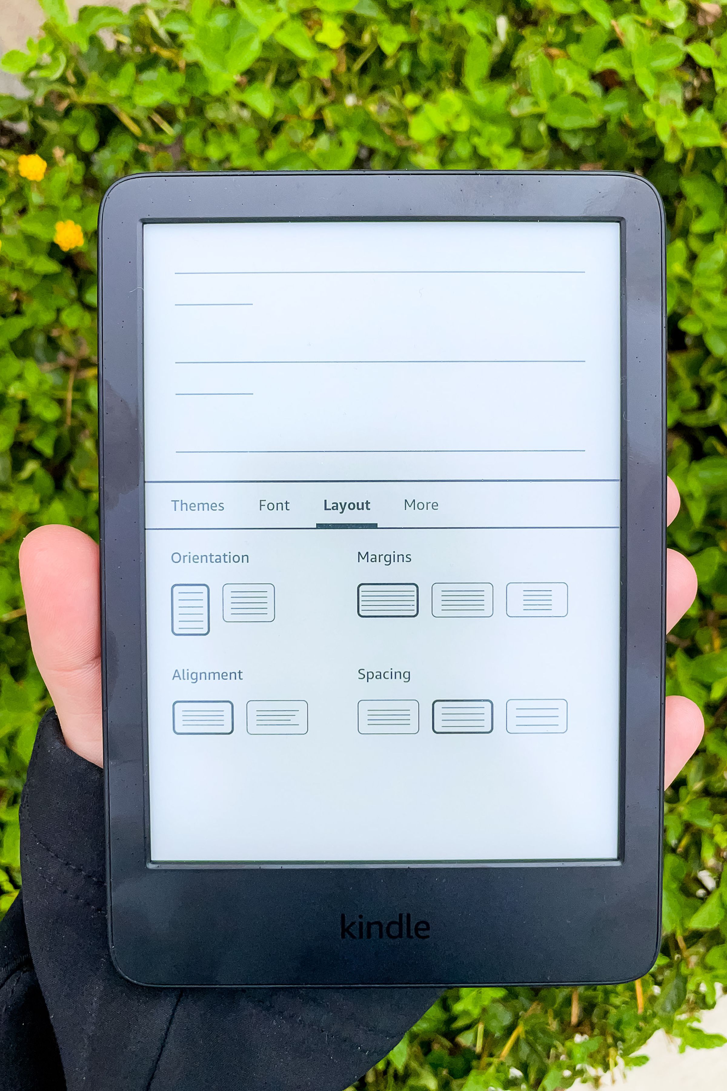 A hand holding the Kindle and displaying a menu with options to change the orientation, alignment, spacing, and margins.