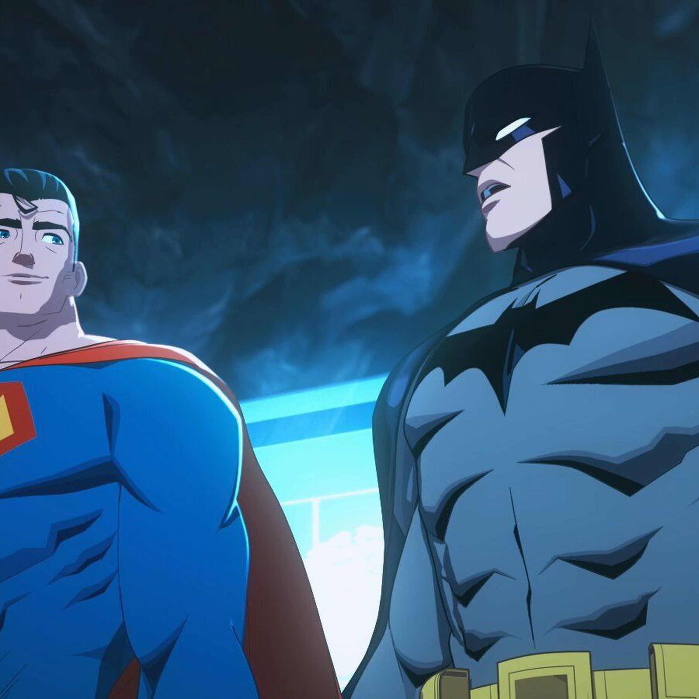 Superman and Batman standing in the Batcave in front of the Batcomputer, which is lighting them both from the back.