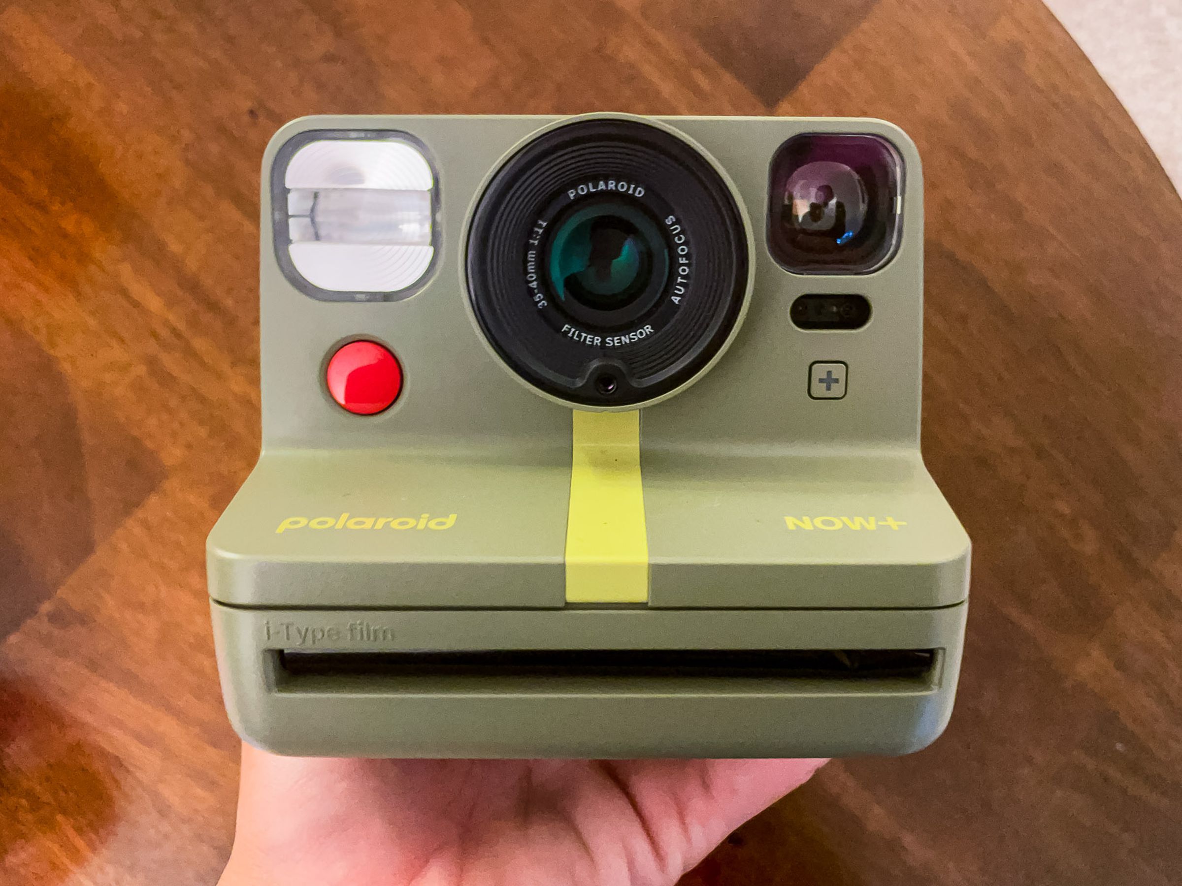 A closeup of a green second-gen Polaroid Now Plus held up against a brown background.