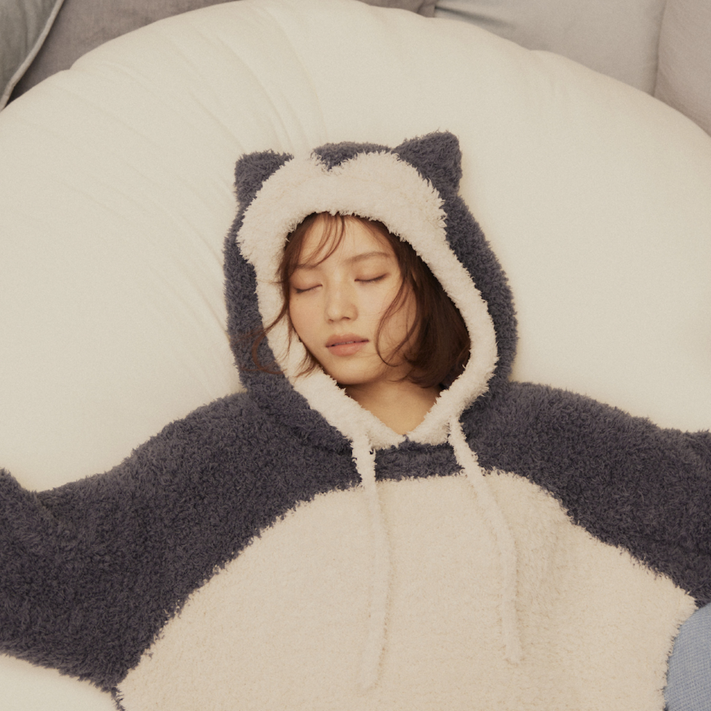 A medium shot of a sleeping woman wearing a fuzzy hoodie, and stretching her arms out while laying down in a bed.