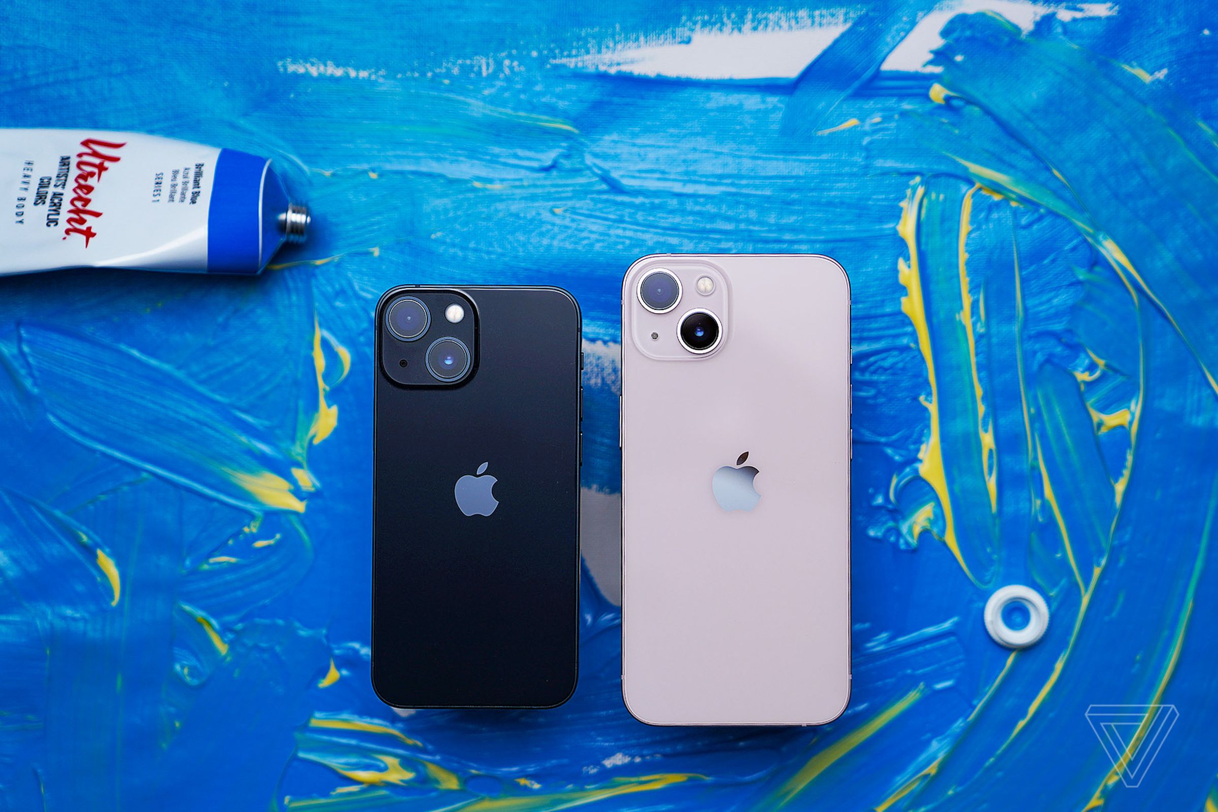 Photo of an iPhone 13 Mini next to a regular-sized iPhone 13 on a blue painted background.