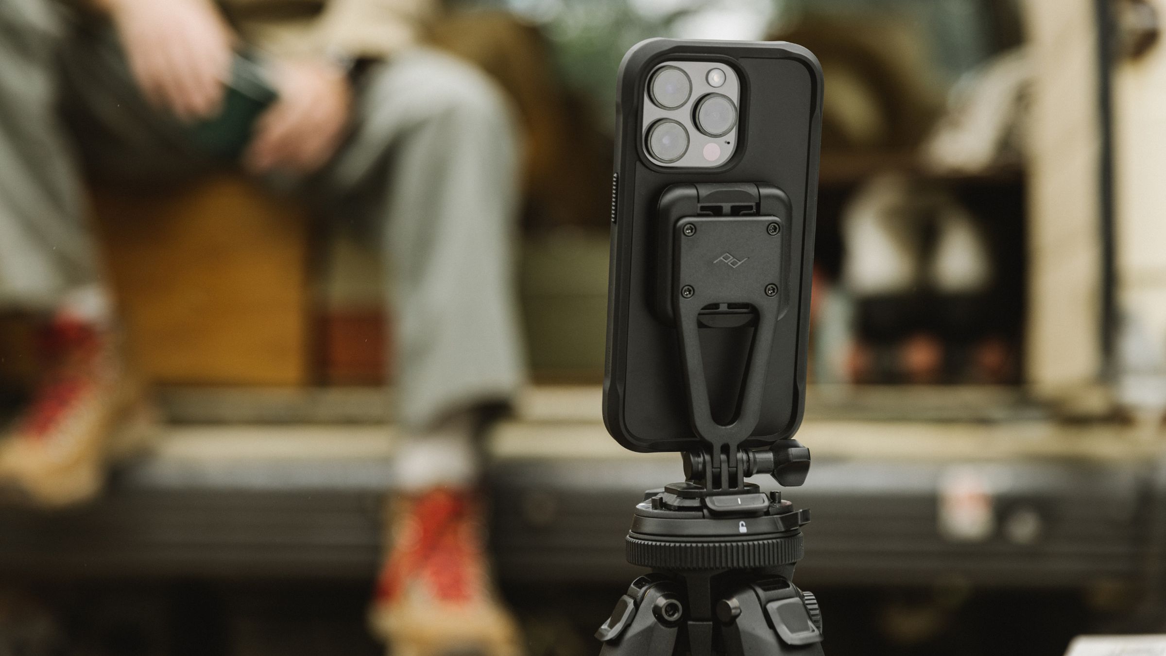 A lifestyle picture of the Nomad x Peak Design rugged iPhone 14 Pro case. The case is attached to a tripod stand outside of a camping van.