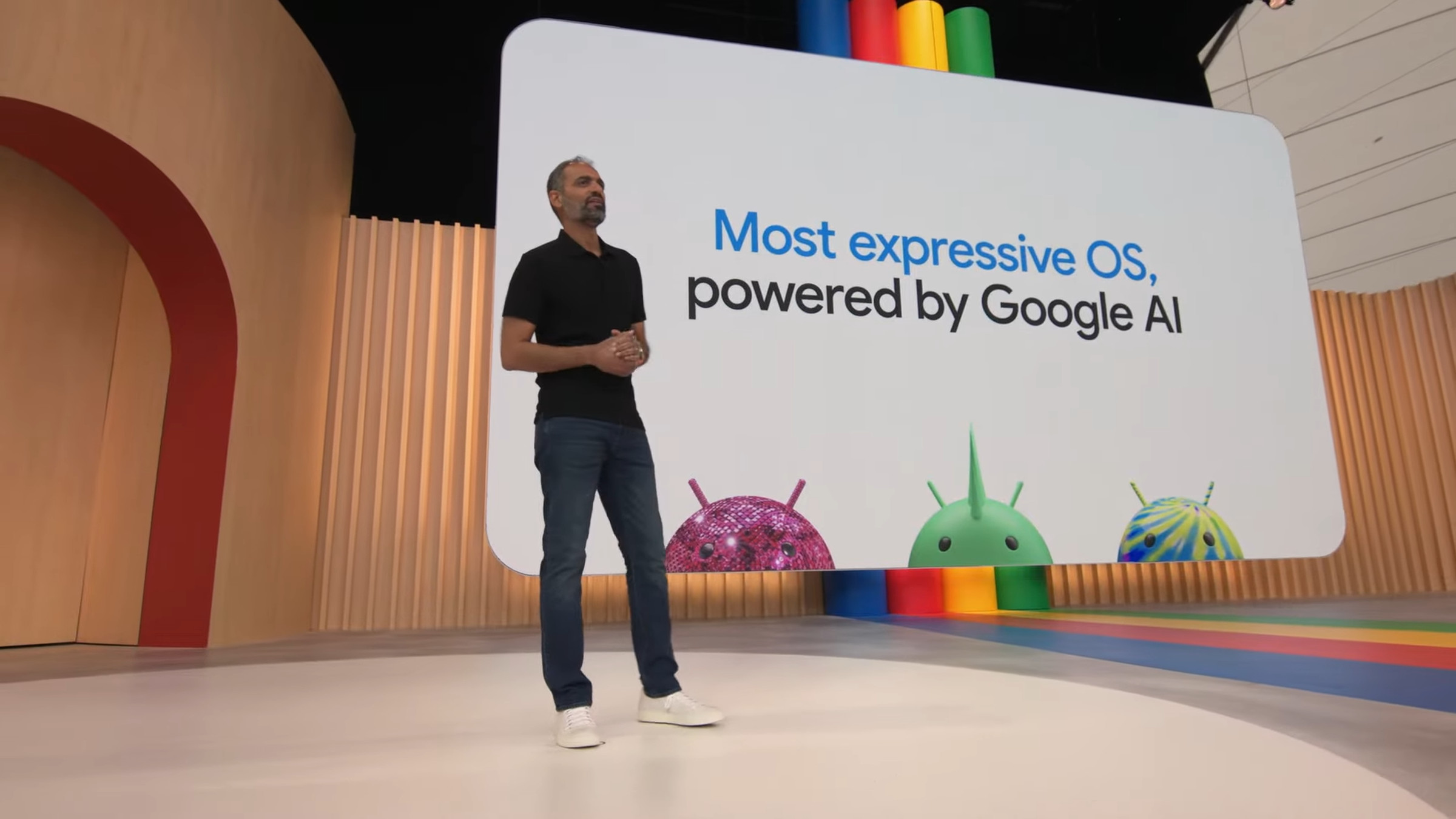 At Google I/O 2023, a slide shows three of the 3D Android heads. Google executive Sameer Samat is speaking onstage.