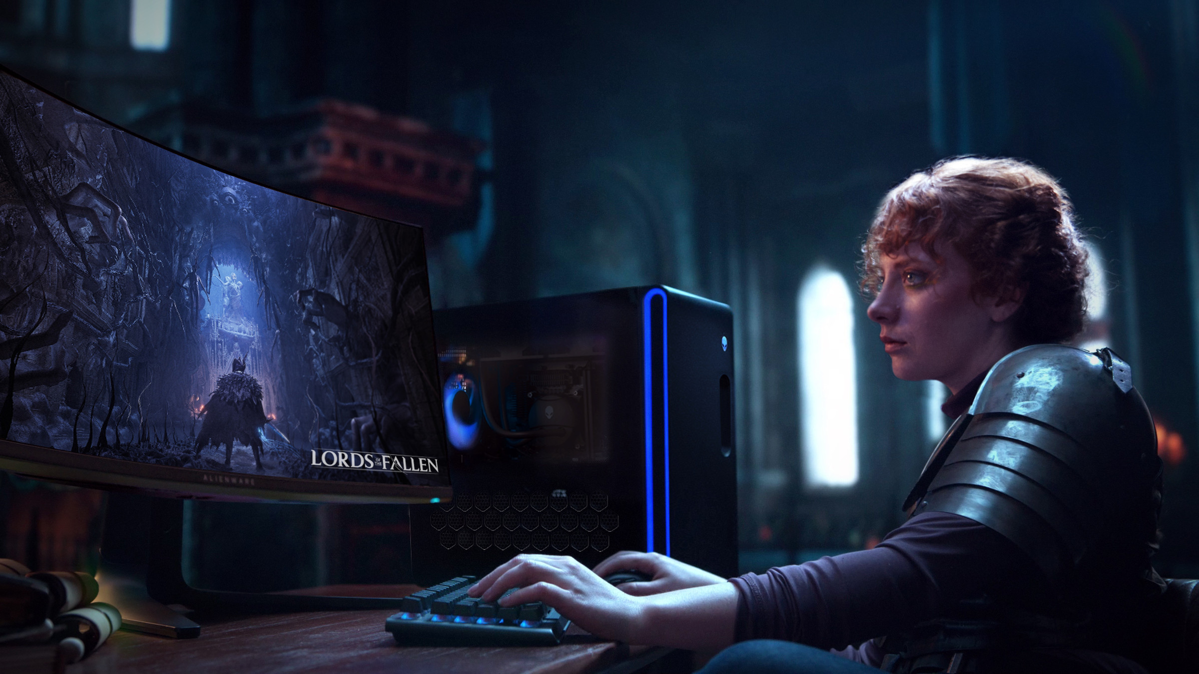 A person playing a game with the Aurora R16 next to their monitor on the desk, picture taken from the side.