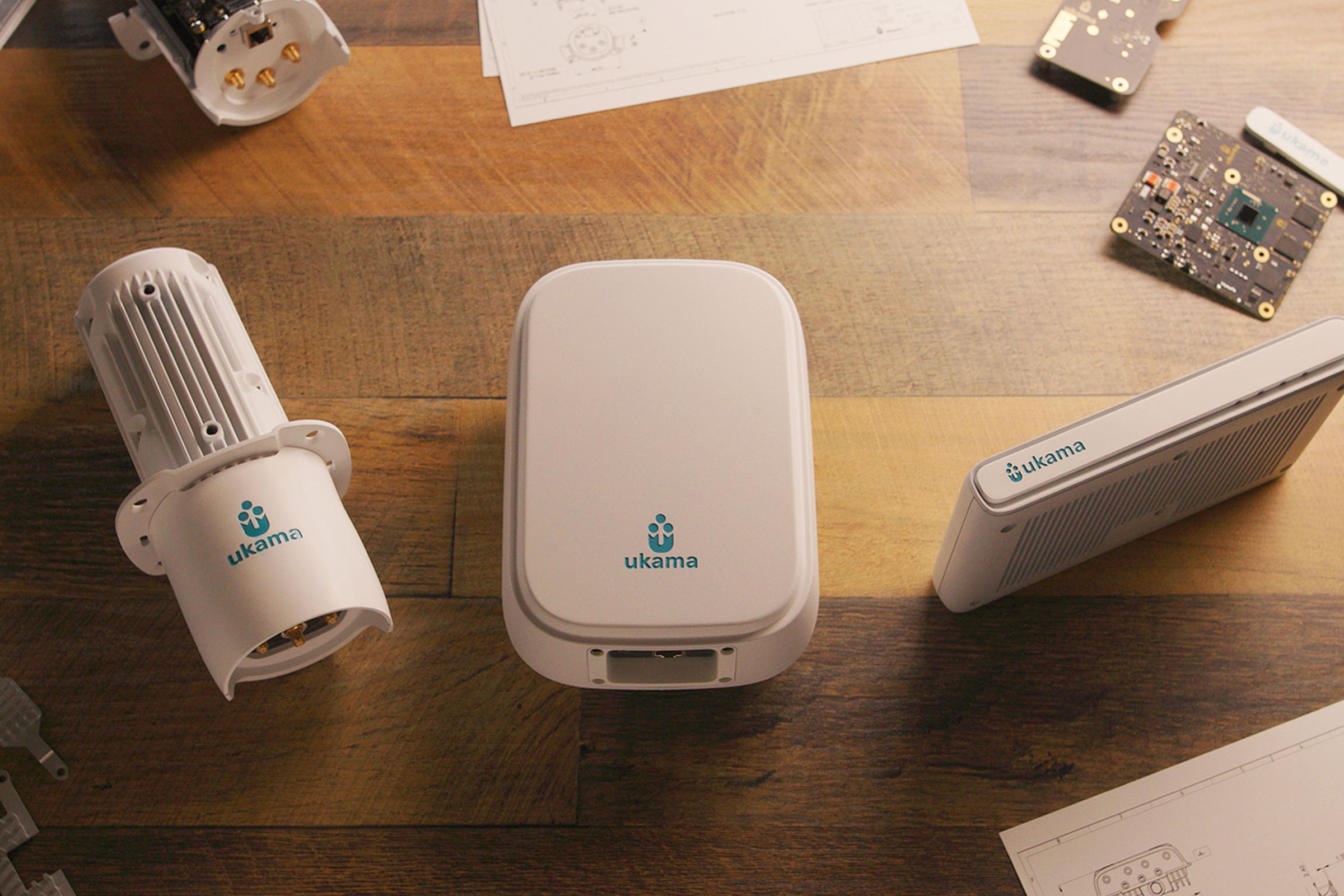 Image of several white plastic devices on a wood table — one somewhat cylindrical, one large rectangular one, and a small, book-like one.