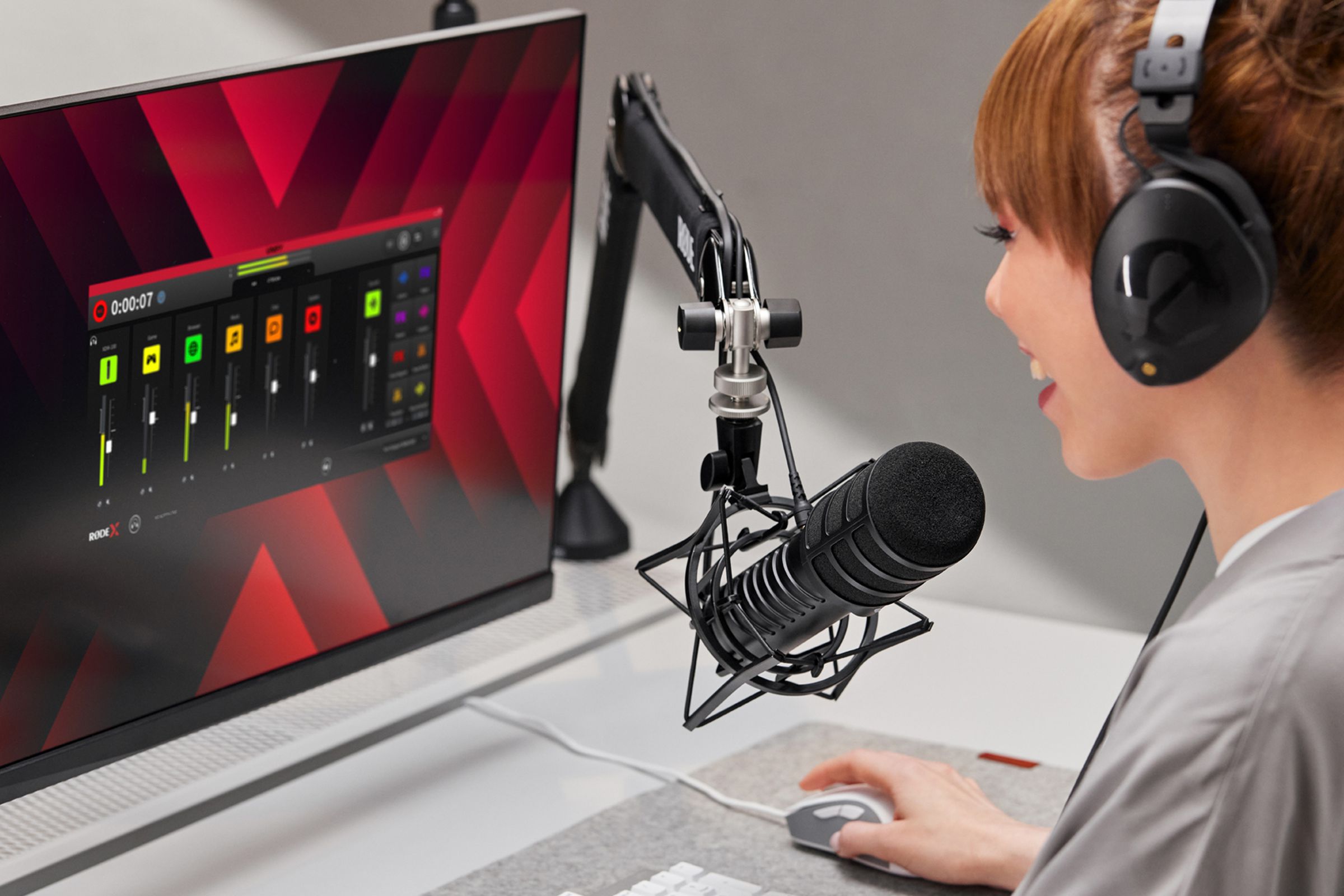 Someone using a Rode X microphone at a desktop PC. The monitor is displaying Rode X Unify mixing software.