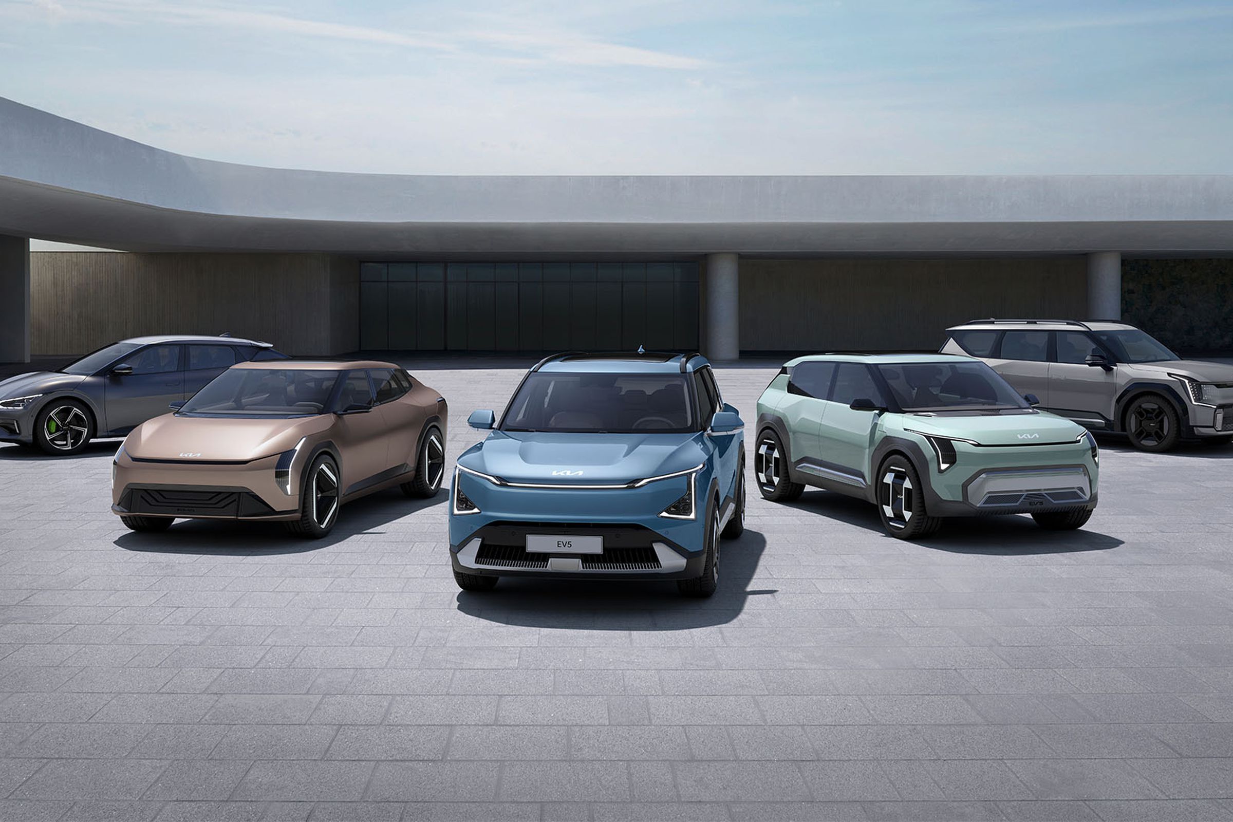 five electric kia vehicles fanned out in a modern architecture area with stone brick flooring