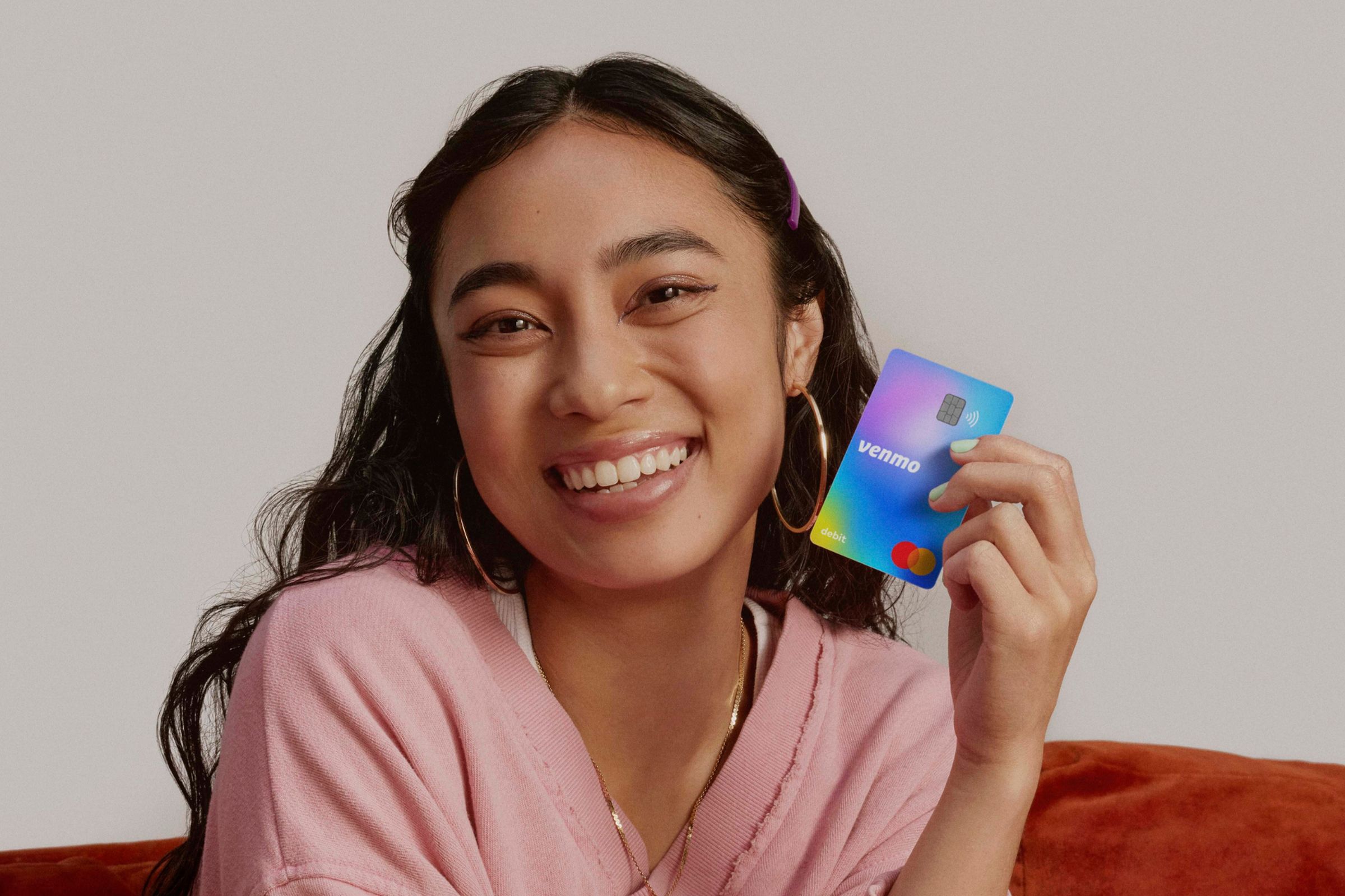 A young teenager smiling while holding a Venmo Teen Debit Card.
