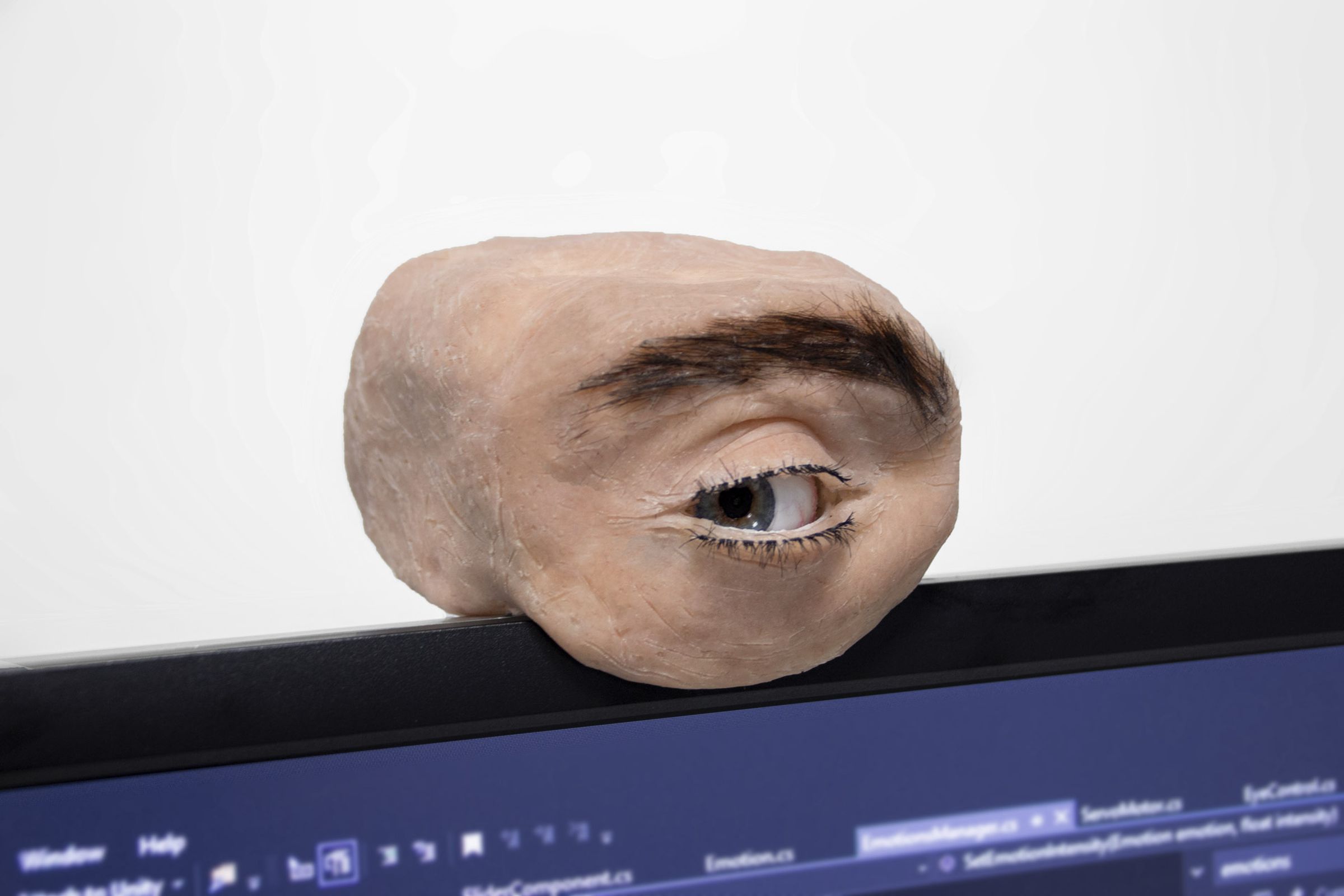 A hunk of synthetic flesh with an eyeball and eyebrow, plopped on top of a screen where a webcam would go. The eye is looking to the left.