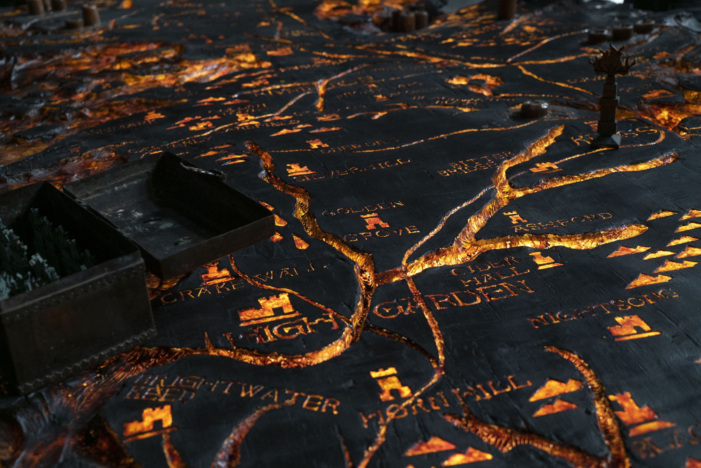 A wooden table into which a map is carved of Westeros. The carved, etched grooves of the map glow golden with a warm light.
