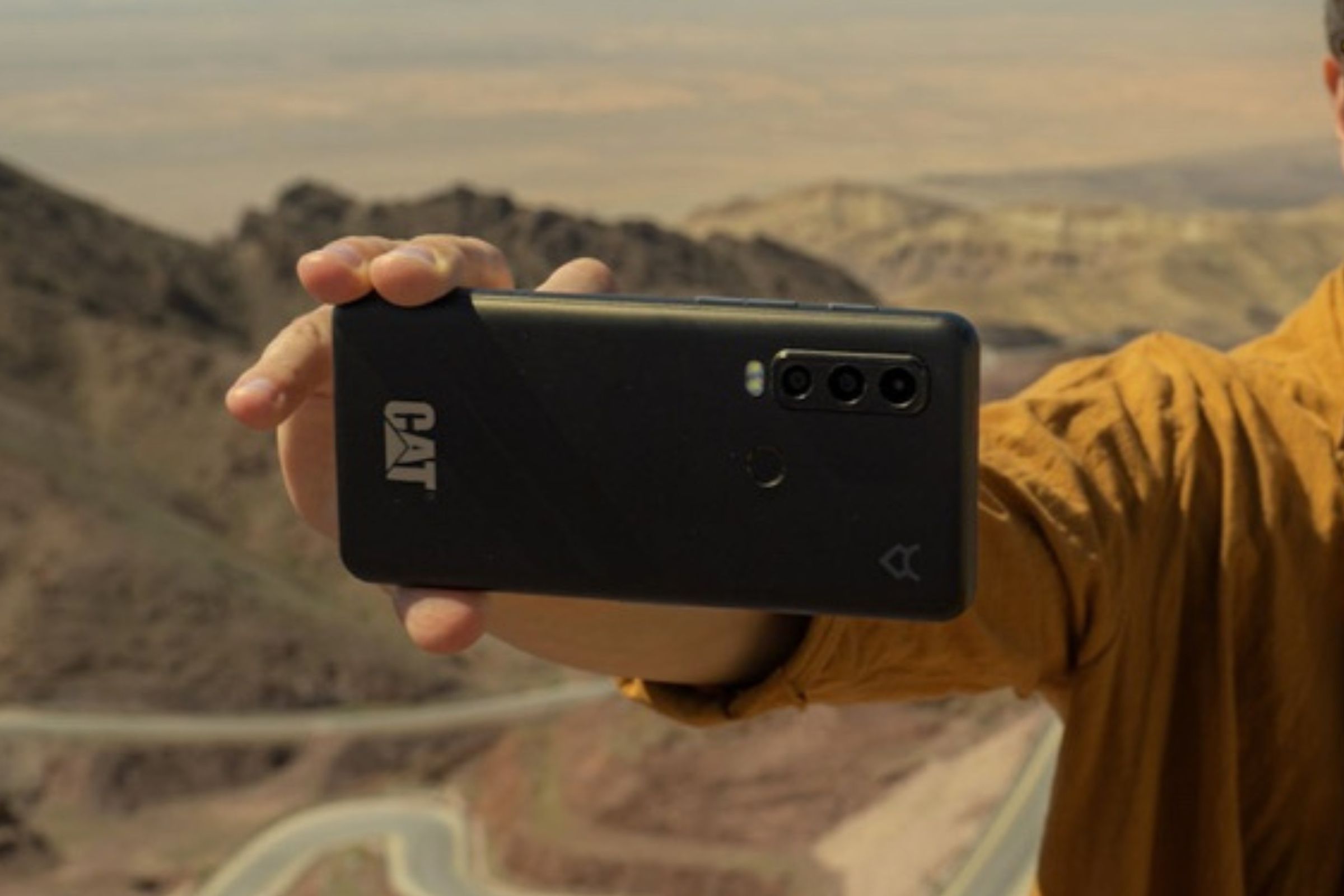 Someone holding a Cat S75 smartphone in a rocky, outdoor environment.