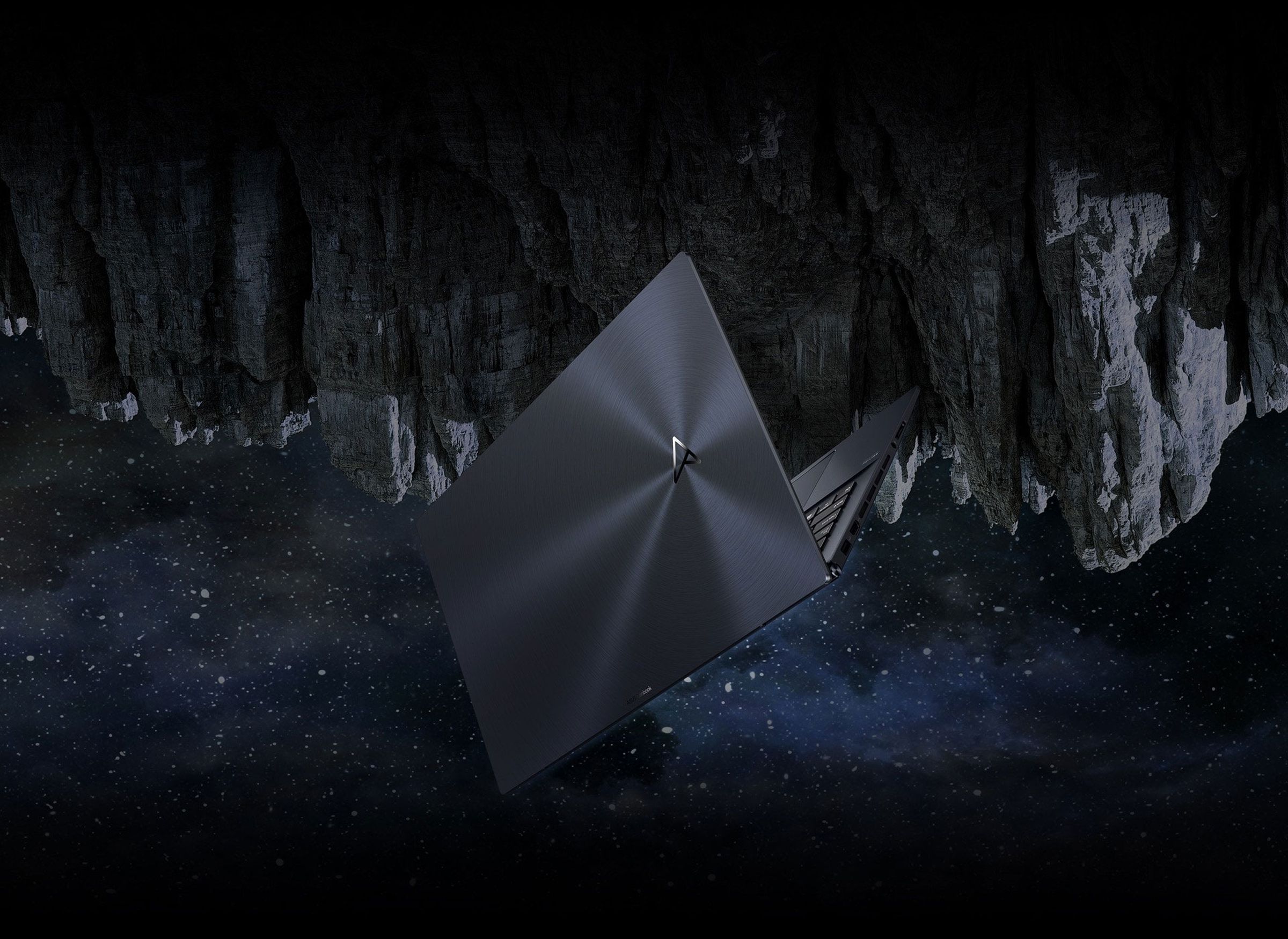 The Zenbook Pro 17 seen from the back, half open, in front of an upside-down mountain at night.