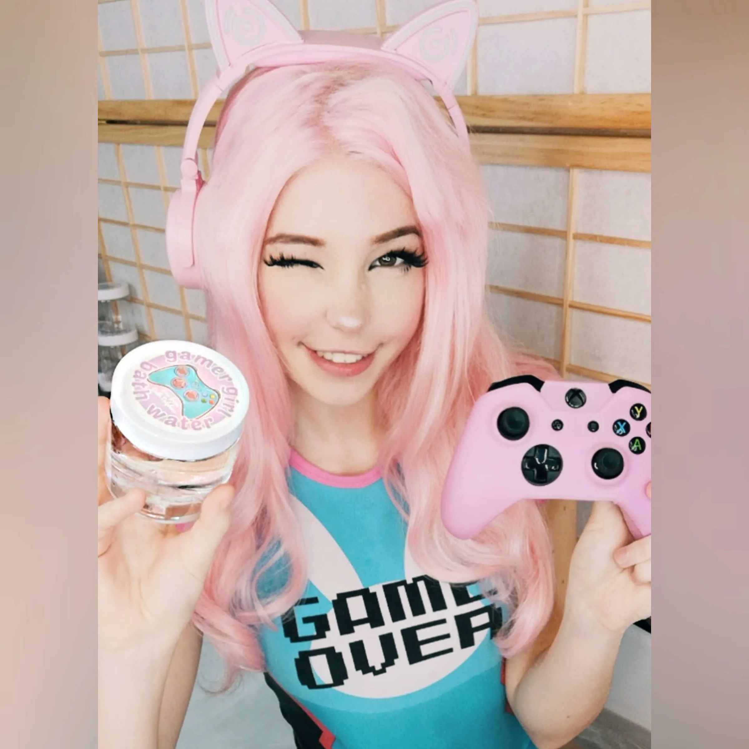 Photo of Belle Delphine, an adult content creator, sitting in a bathtub in a bathing suit holding up a controller and a jar of her bathwater.