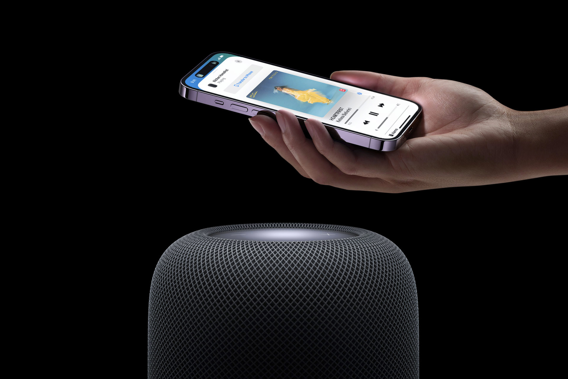 A marketing image of Apple’s second-generation HomePod with an iPhone being held above it.