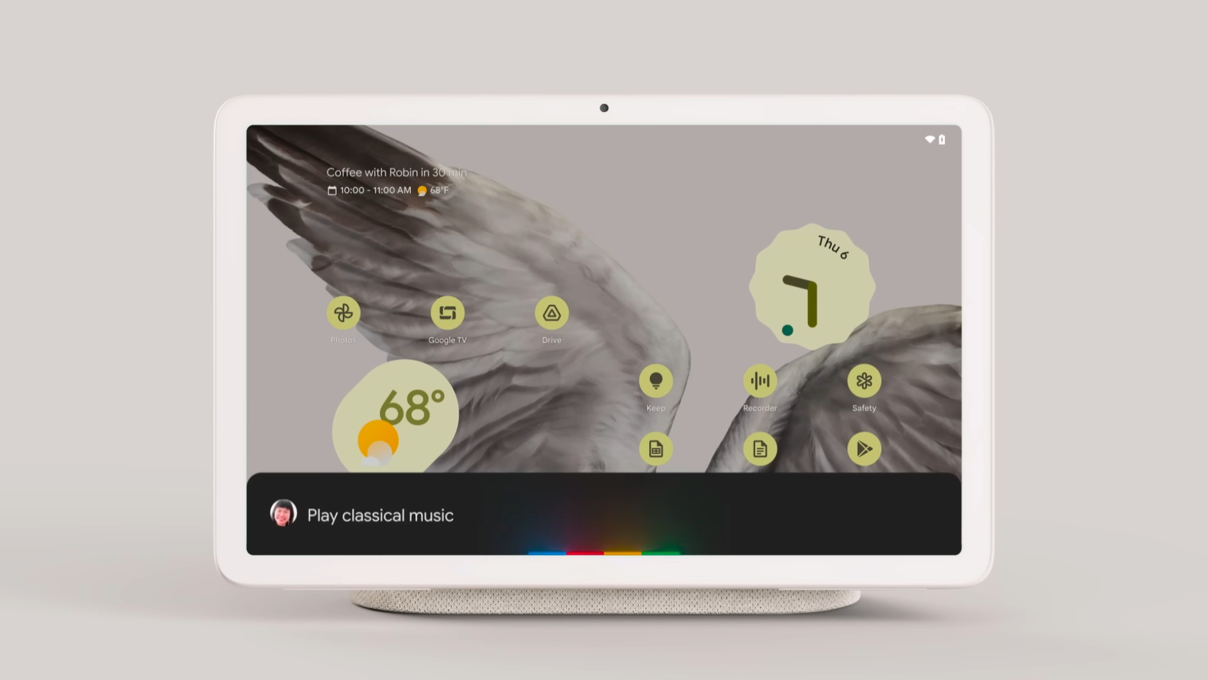 Photograph of a Nest Hub-like tablet on a speaker dock, displaying a Google Assistant toast at the bottom.