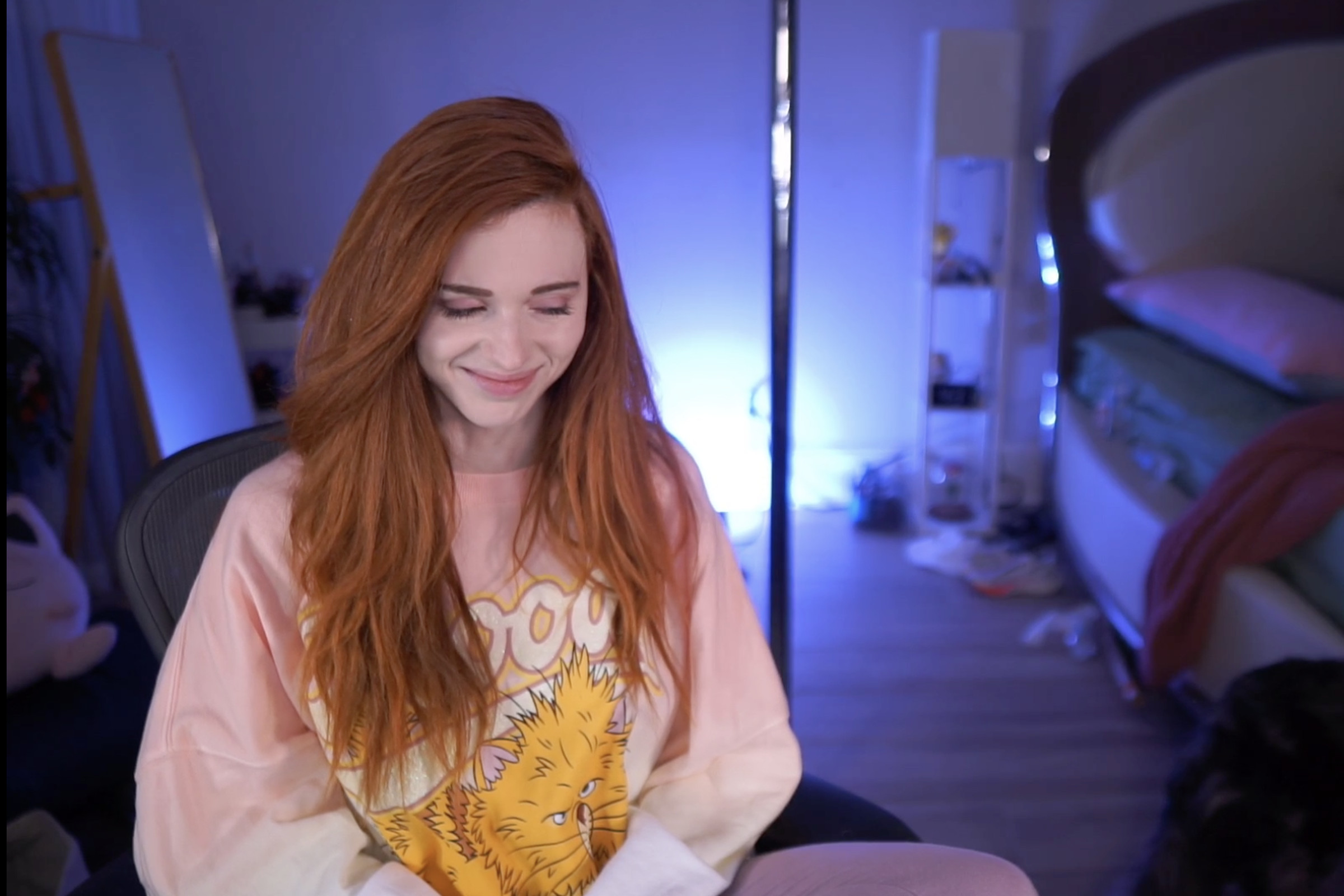 Image of Twitch streamer Kaitlyn “Amouranth” Siragusa a woman with long red hair dressed in a pink hoodie with an orange fuzzy creature on it smiling happily.