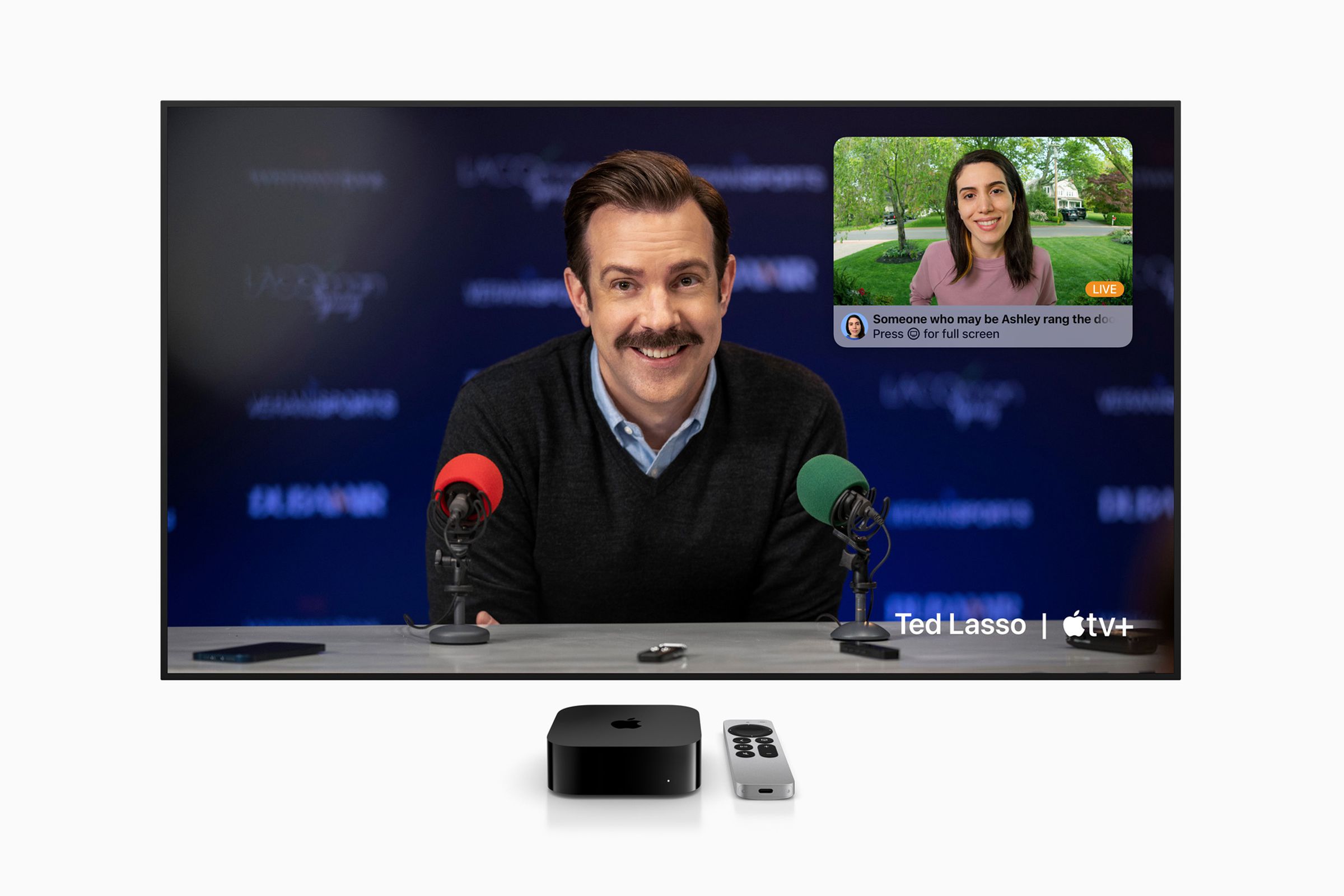 Photo of the new Apple TV sitting next to an Apple TV remote, both of which are under a TV screen displaying Ted Lasso.