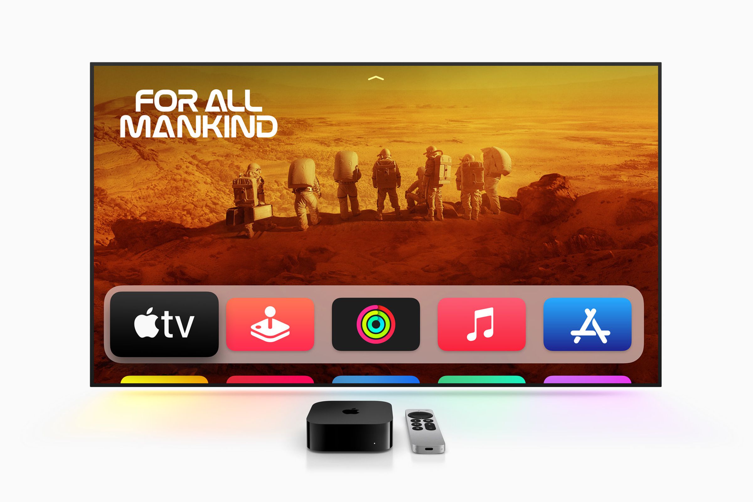 The new Apple 4K TV streaming box alongside its Siri Remote, with a TV turned on.