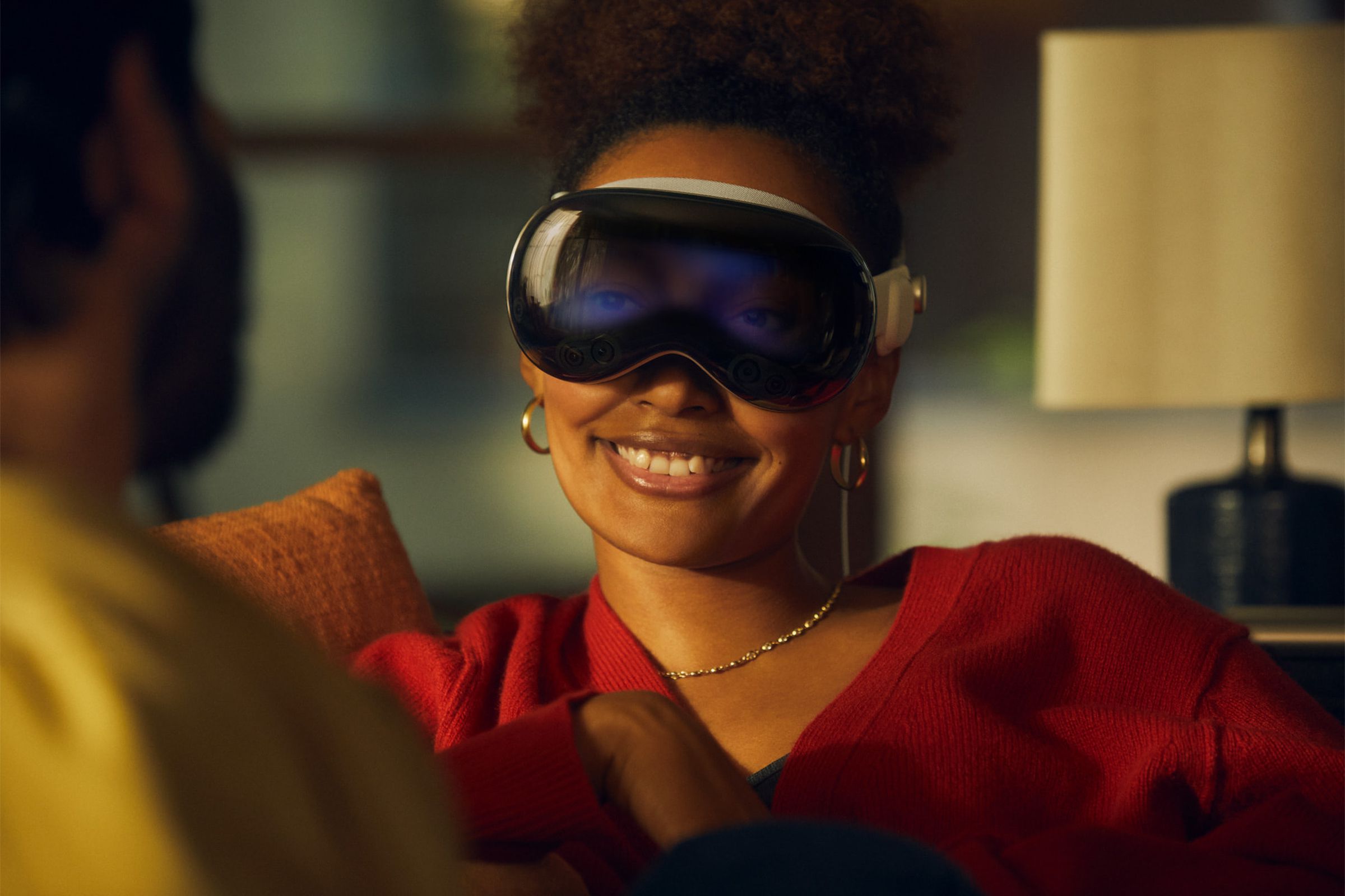 A close-up image of a woman talking to someone on a couch while wearing the Apple Vision Pro.