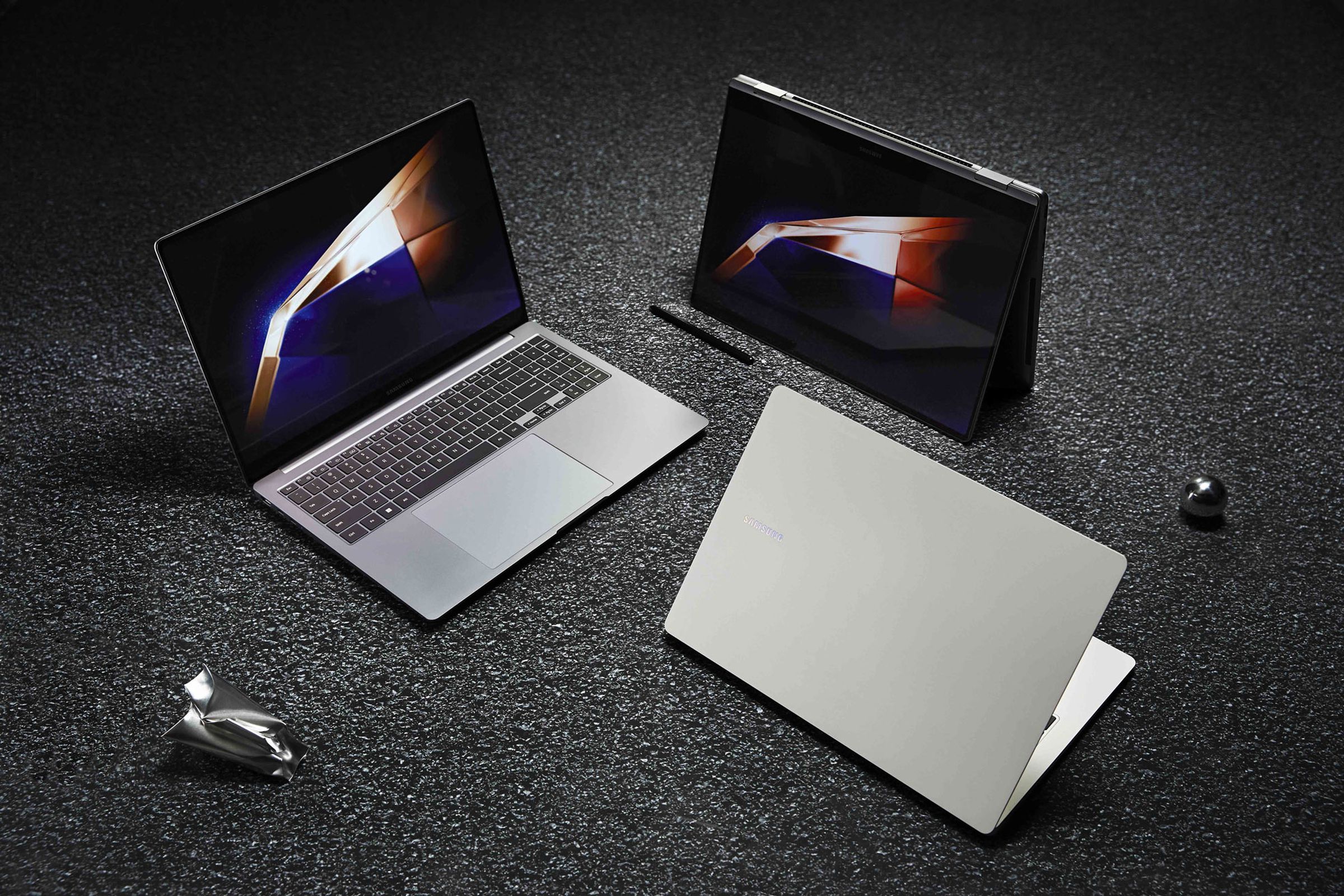 A group of three silver laptops arranged in a circle against a dark gray background.